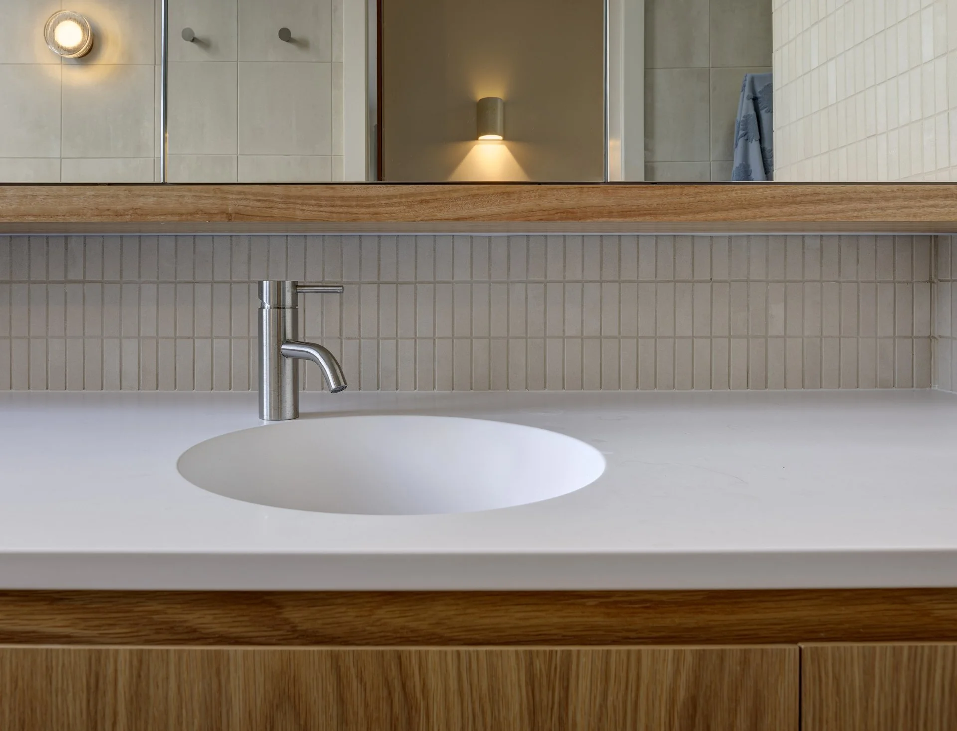 Modern bathroom sink with a round integrated basin, stainless steel faucet, and stone coloured tiled splashback.