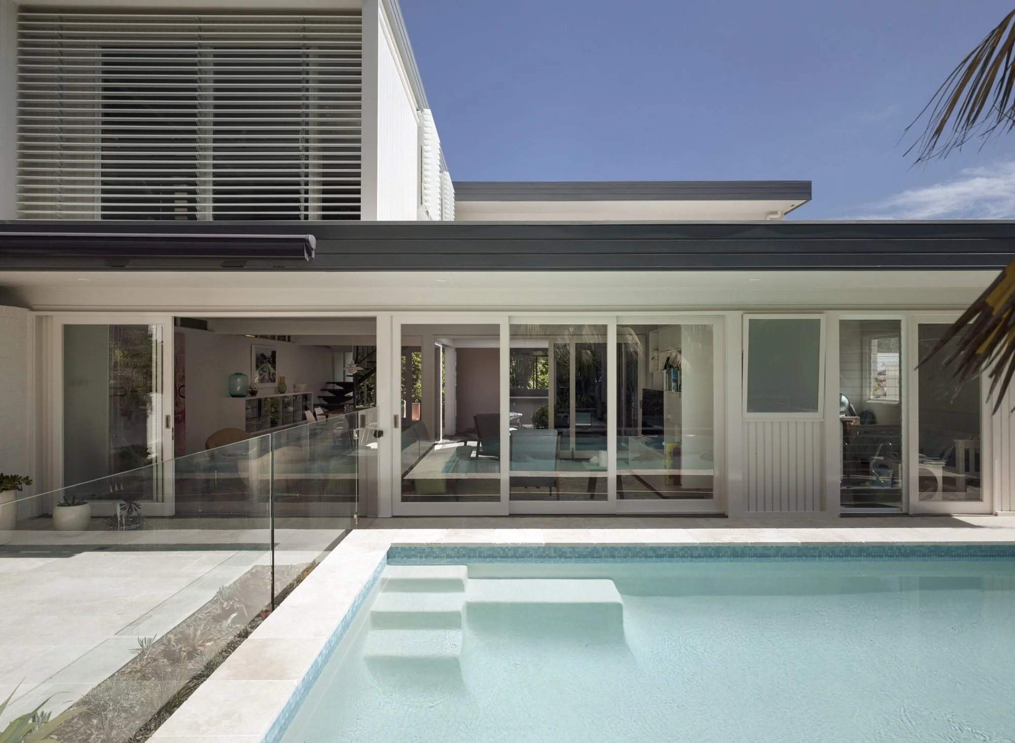 Modern house exterior with a swimming pool, glass sliding doors, and large windows, featuring a minimalist design.