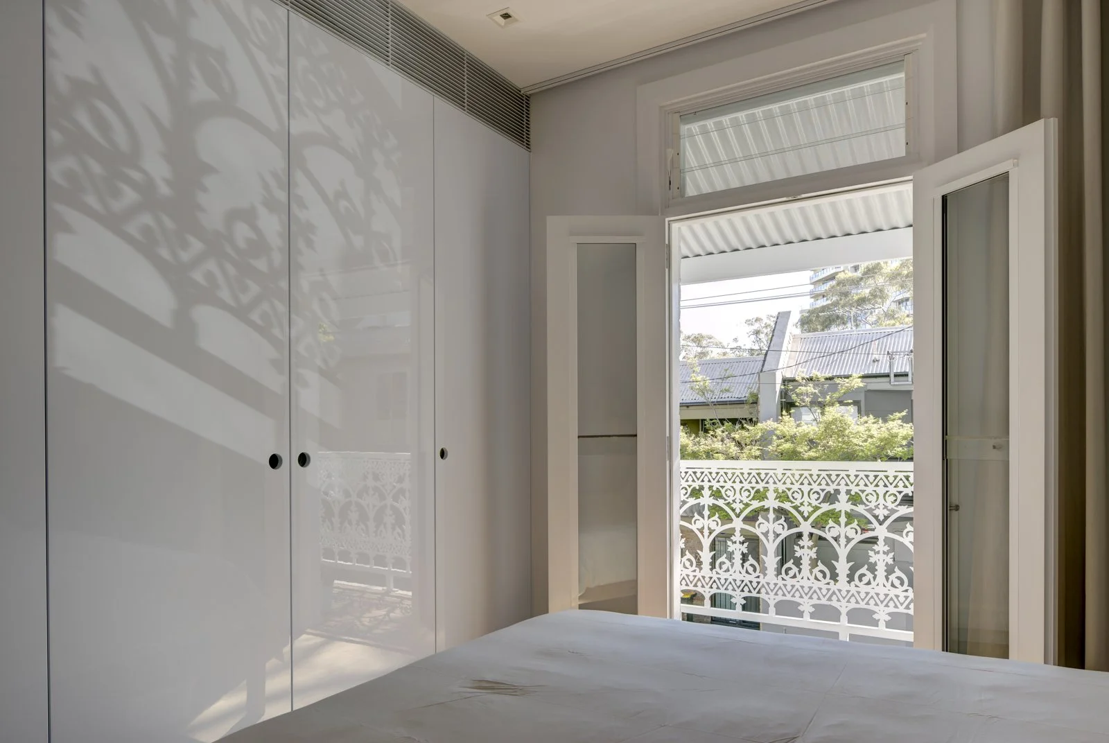 Bedroom interior with open white door leading to balcony with heritage  railing, reflection of the railing pattern on closet doors.
