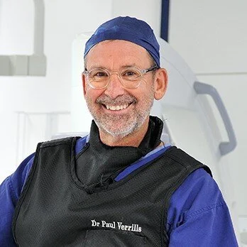 Smiling man in medical scrubs and surgical cap in a clinical setting.