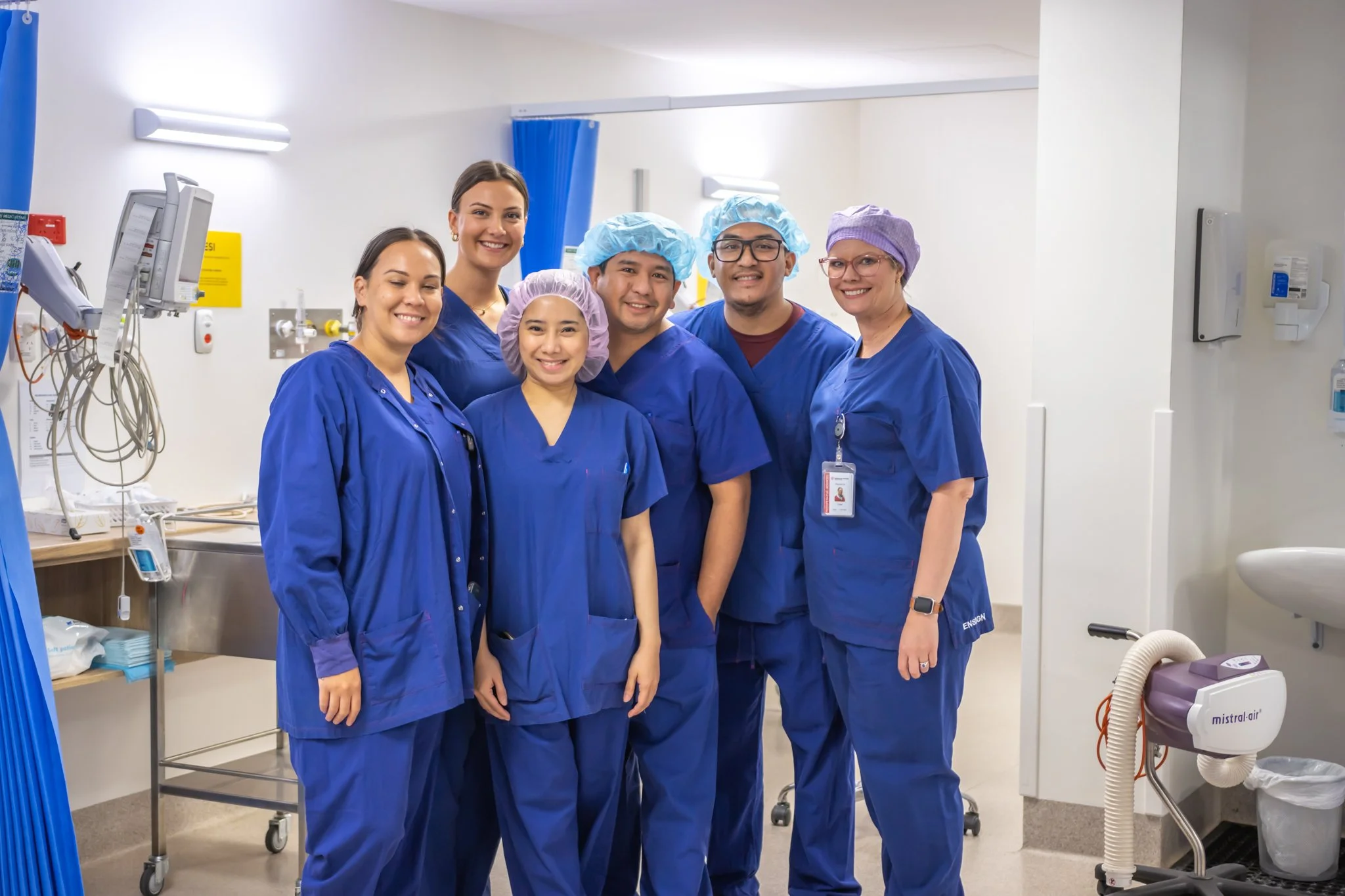 Group of medical staff in blue scrubs smiling in a hospital corridor.
