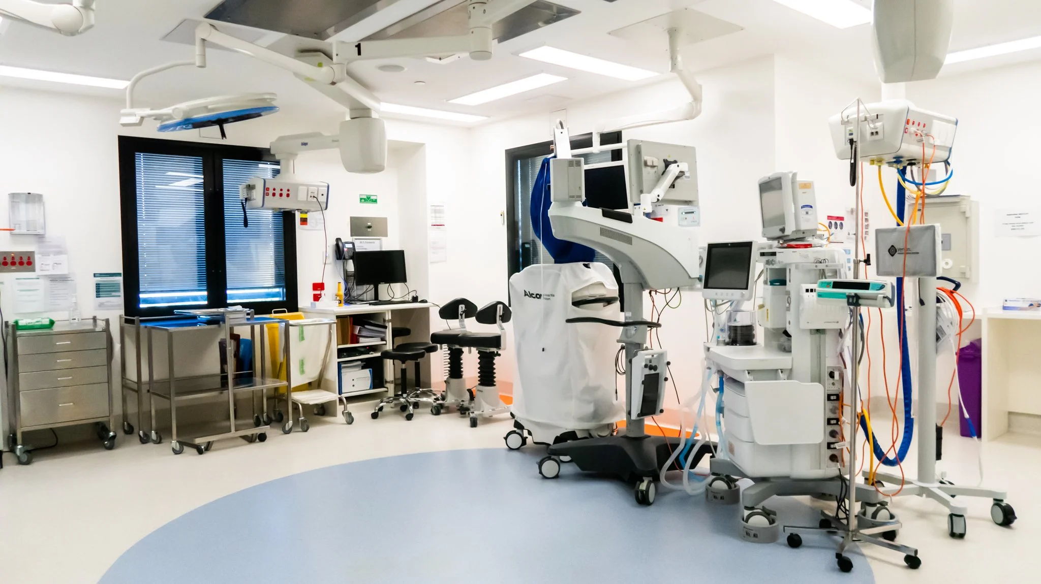 A hospital room with medical equipment, including monitors, infusion pumps, surgical lights, and a patient bed, all in a clean, well-lit environment.