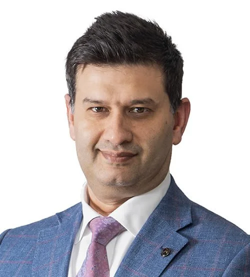 Headshot of a man in a blue suit jacket, white shirt, and purple tie, smiling slightly with a confident expression against a white background.