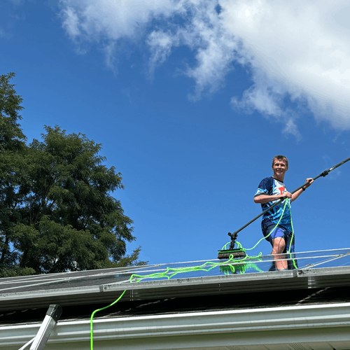 Adam from Lansing Precision Power-Wash standing behind an array of solar panels actively cleaning them according to manufacturer specifications!
