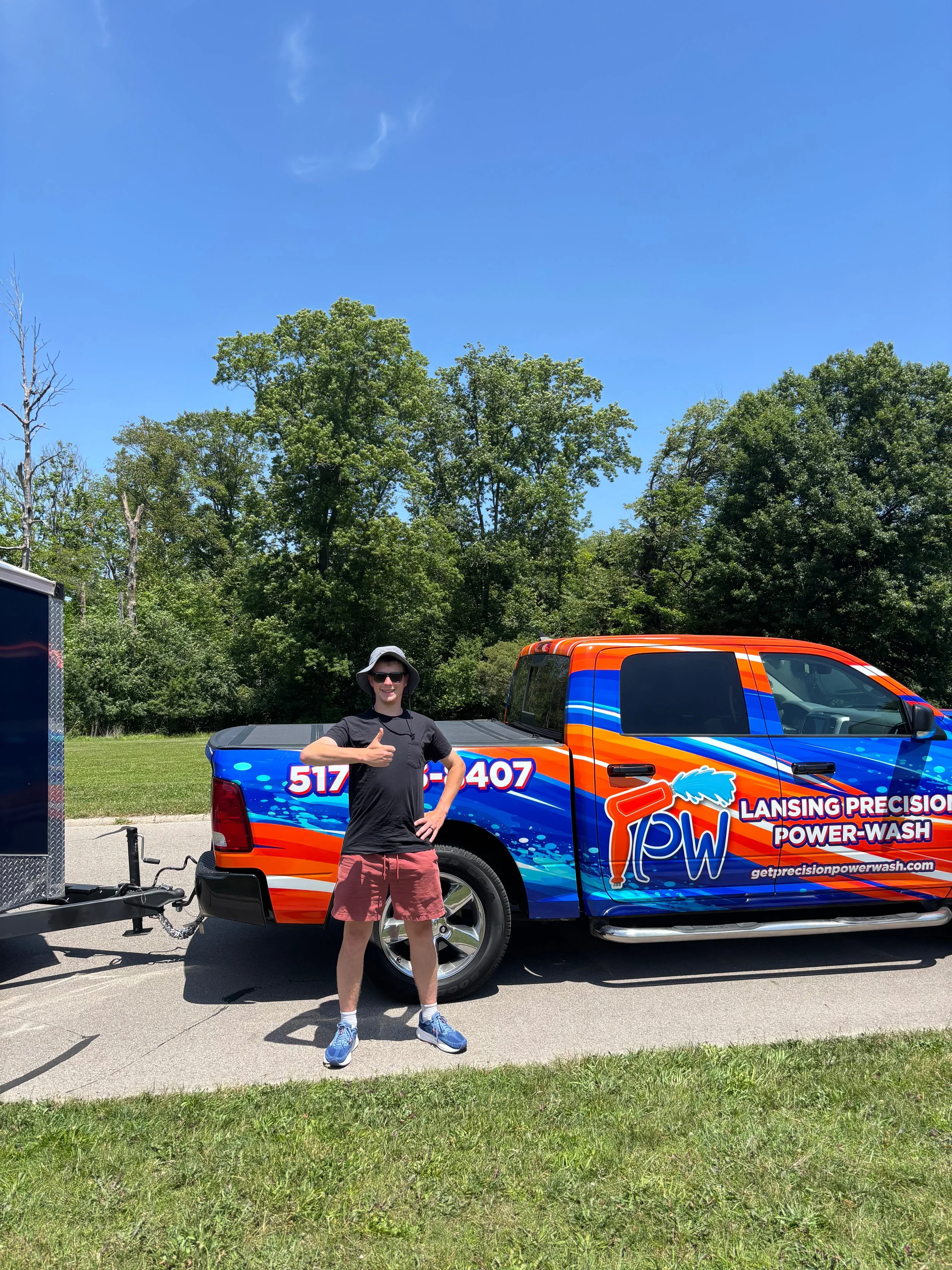 Adam from Lansing Precision Power-Wash standing his his hand on his hip and thumb up in front of the Lansing Precision Power-Wash wash-mobile