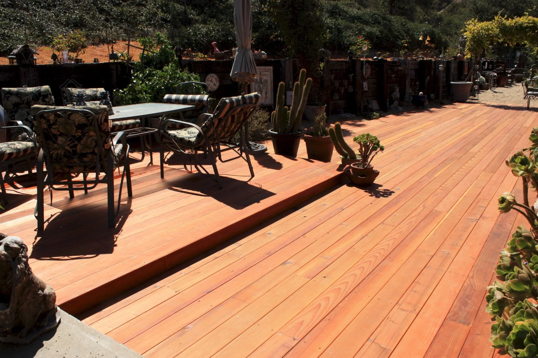 Wooden outdoor patio with patio furniture, potted cacti, and garden decorations under bright sunlight.