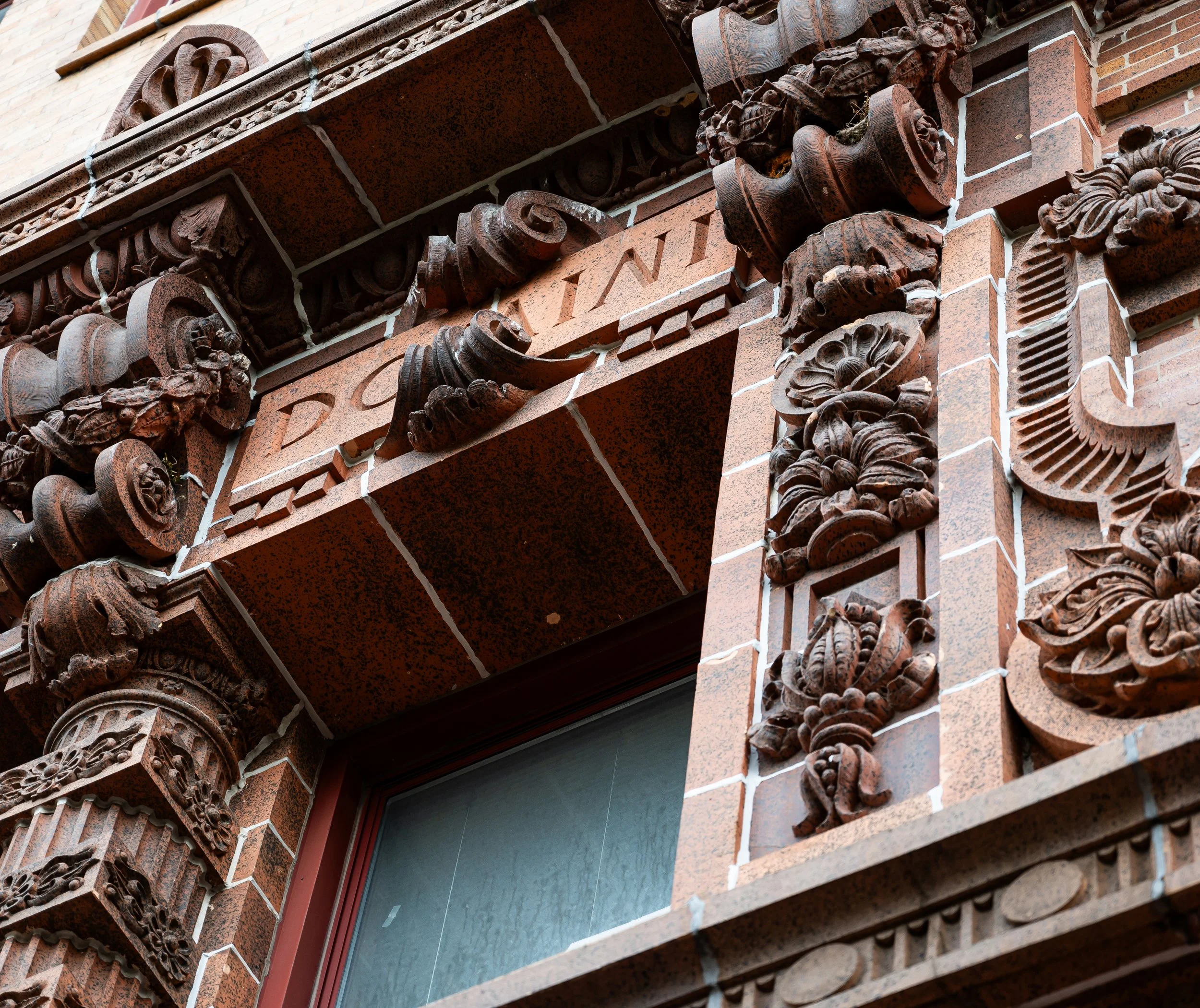 Close-up of ornate brick and terracotta architectural details on a historic building, featuring intricate carved patterns and decorative elements around a window in downtown Anderson, IN. 