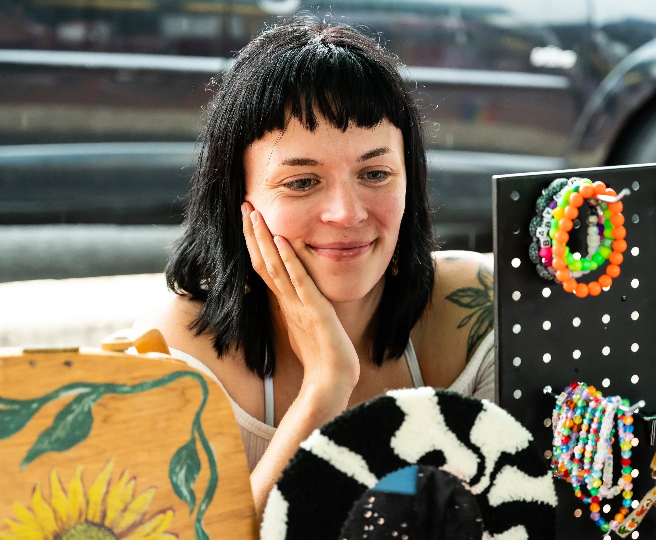 Woman with black hair and a butterfly tattoo looking at jewelry on a display stand.