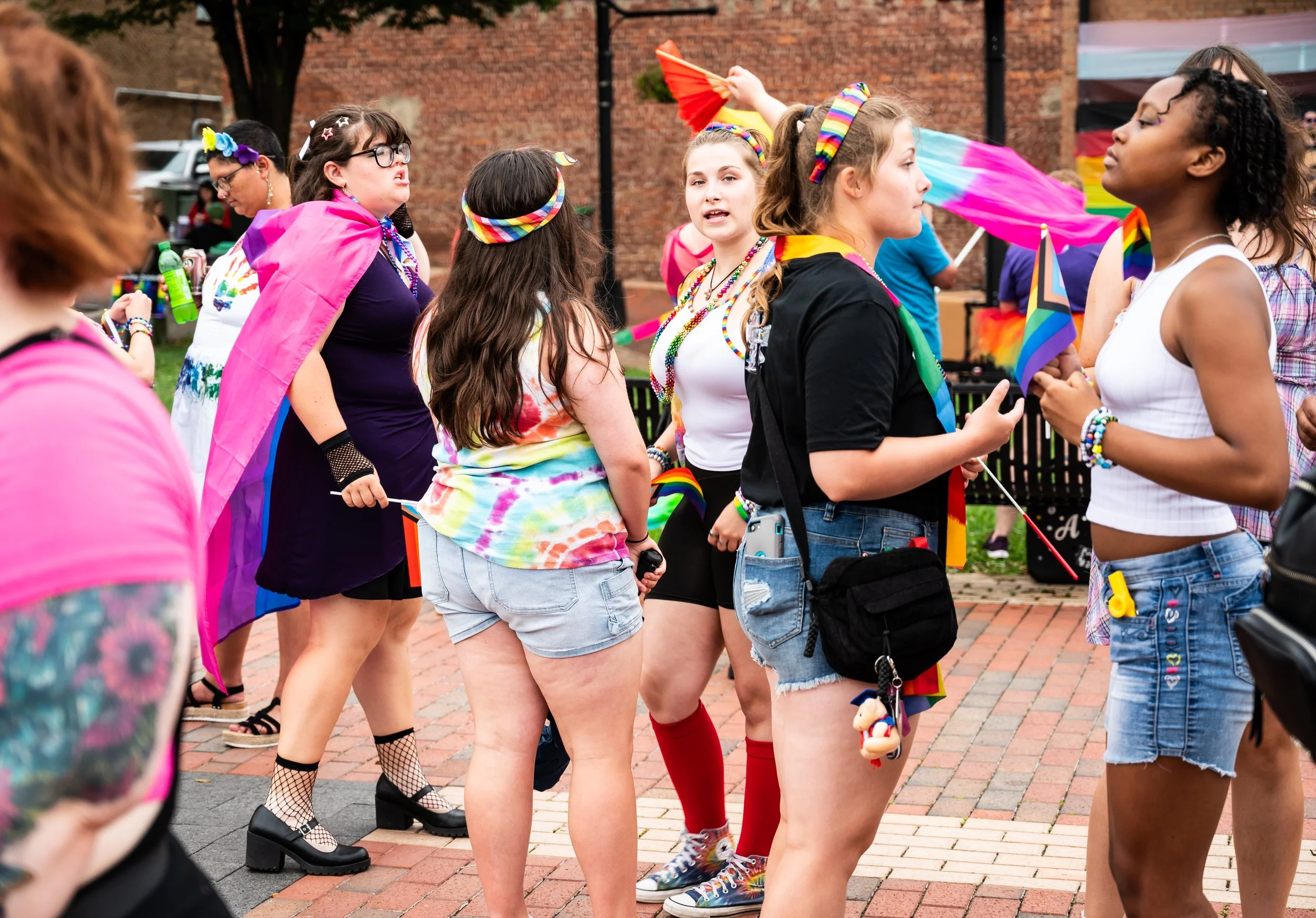 Group of people celebrating LGBTQ+ pride outdoors, wearing colorful clothing and accessories, holding pride flags.