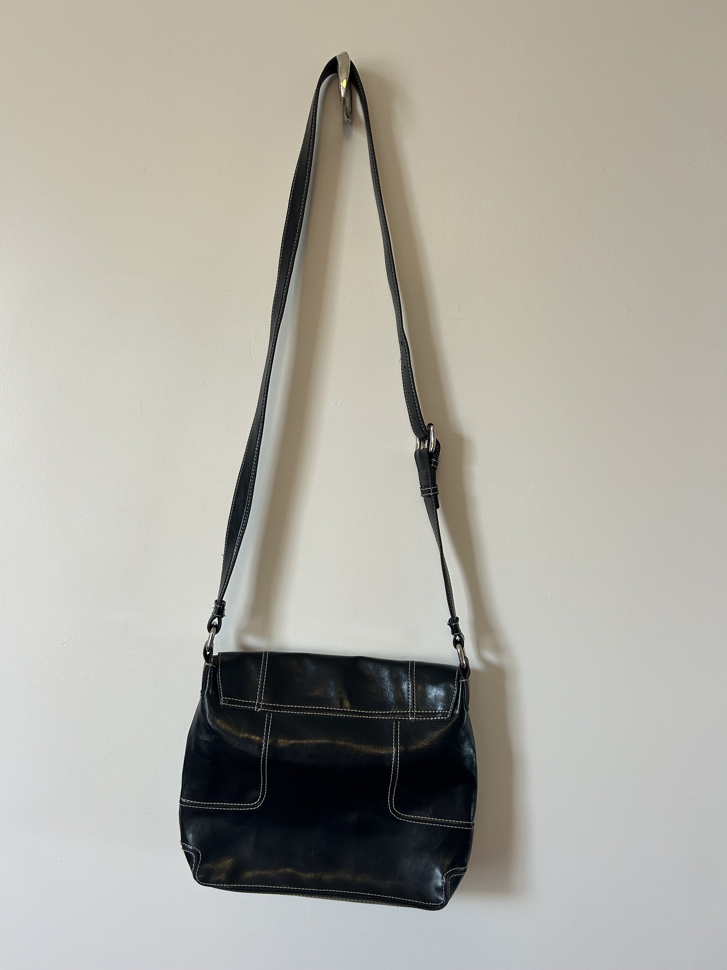 A black handbag with a long cross body strap hanging from a metal wall hook