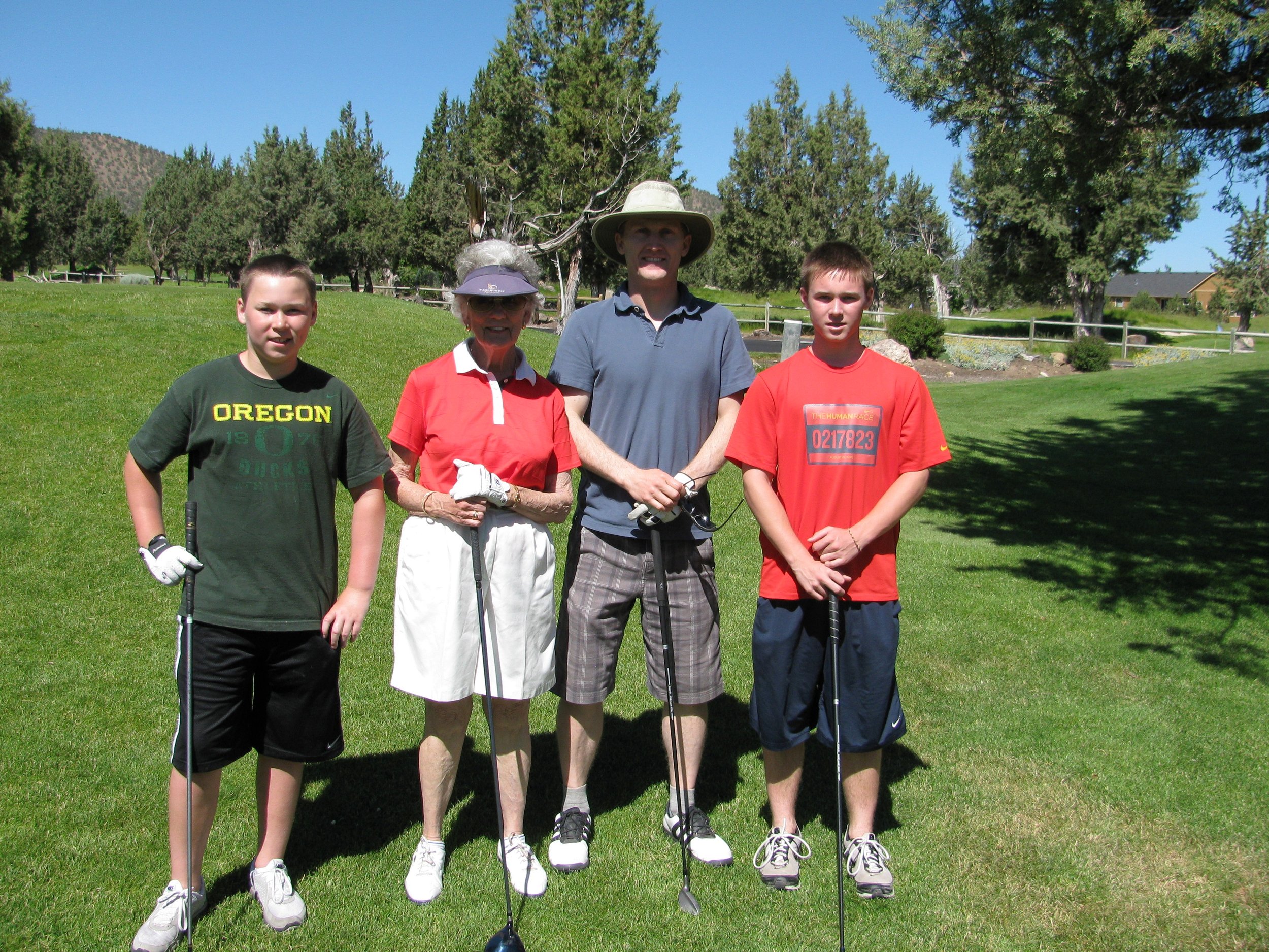 87-year-old woman golfing with her grandsons, modeling lifelong movement and vitality on a sunny day at the golf course.