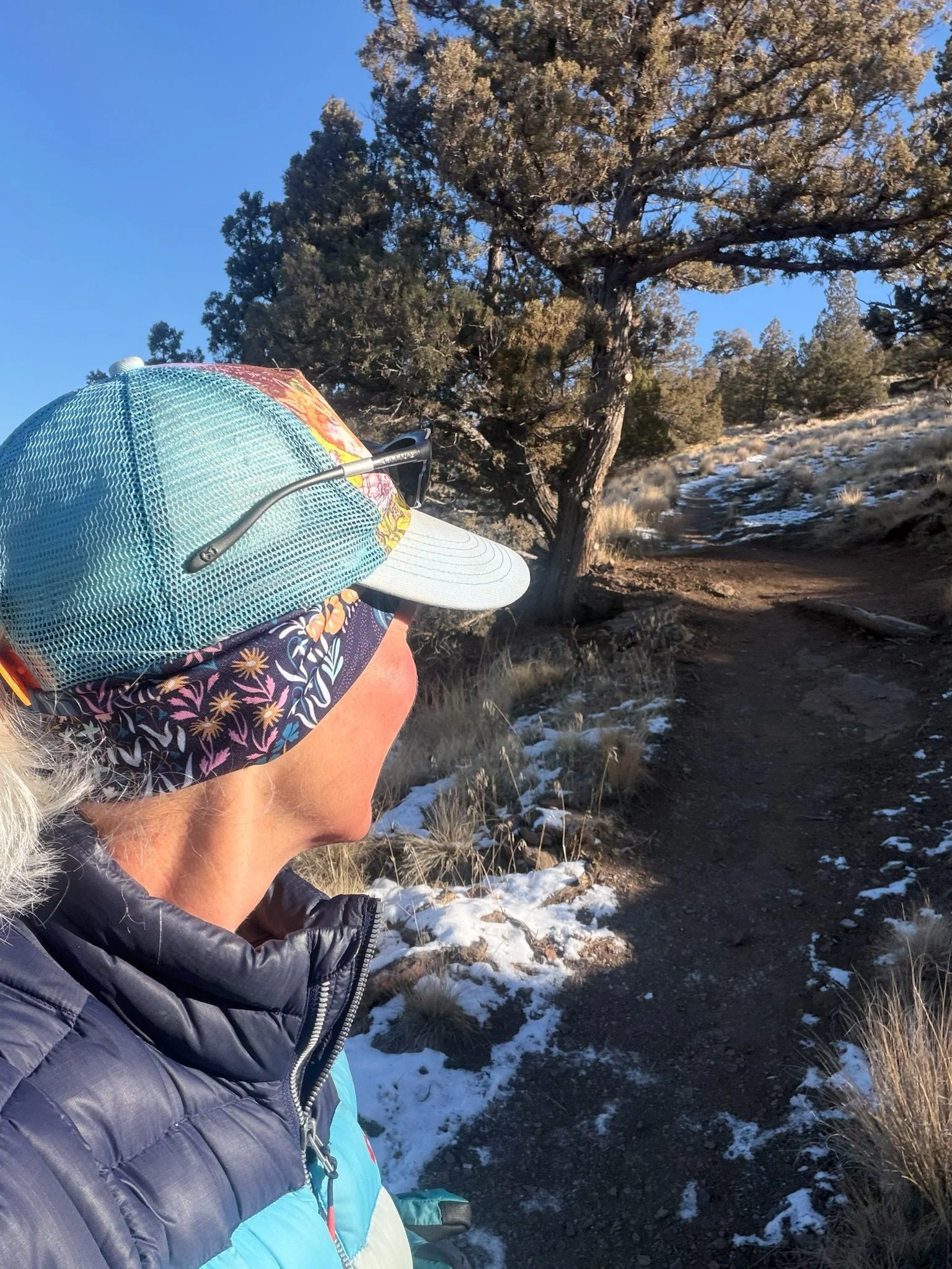 A woman standing on a winter trail, looking ahead along a winding path through trees.