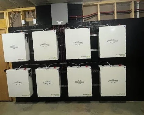 Eight white solar inverters mounted on a black wall in a technical room.