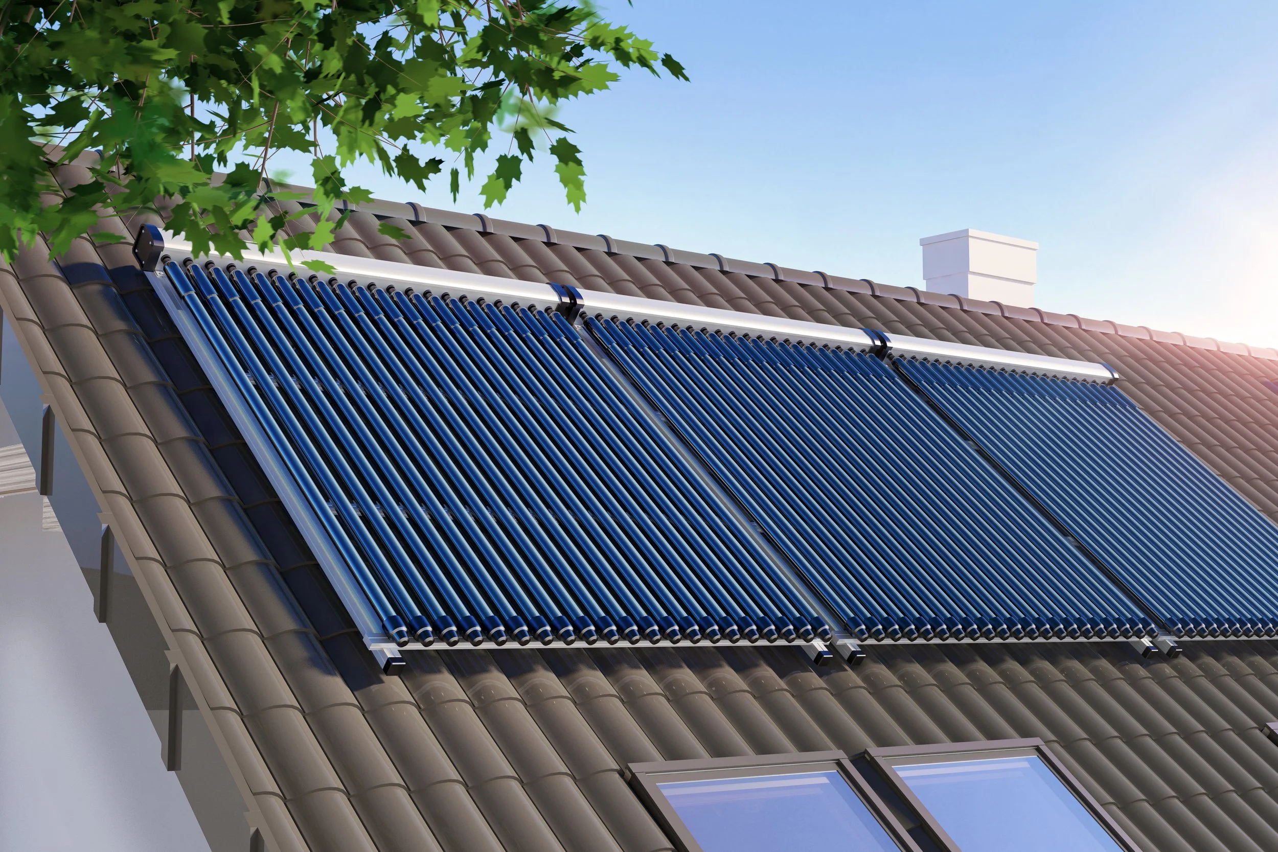 Close-up of a house roof with solar panels installed, with green leaves from a tree in the foreground and a clear blue sky in the background.