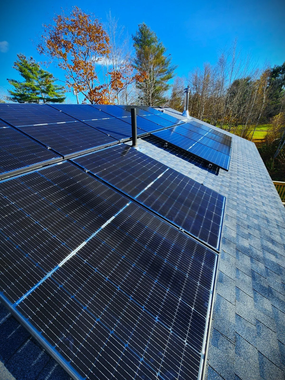 Solar panels installed on a house roof with trees and blue sky in the background.