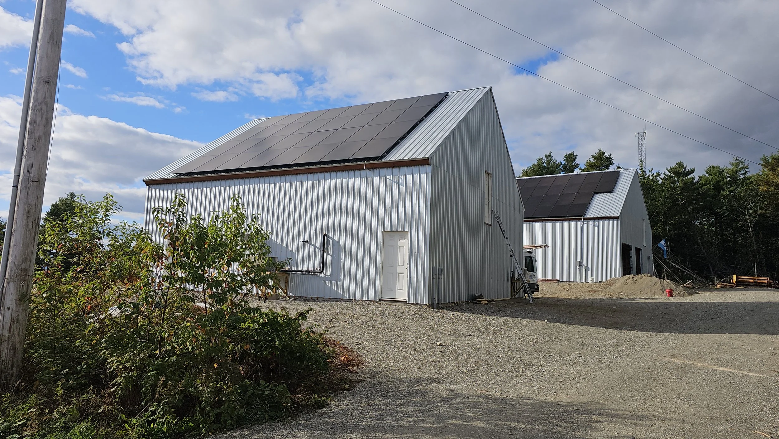 Farm buildings under a partly cloudy sky, with one structure featuring solar panels on its roof.