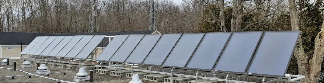 Row of solar panels on rooftops in a residential area with trees in the background.