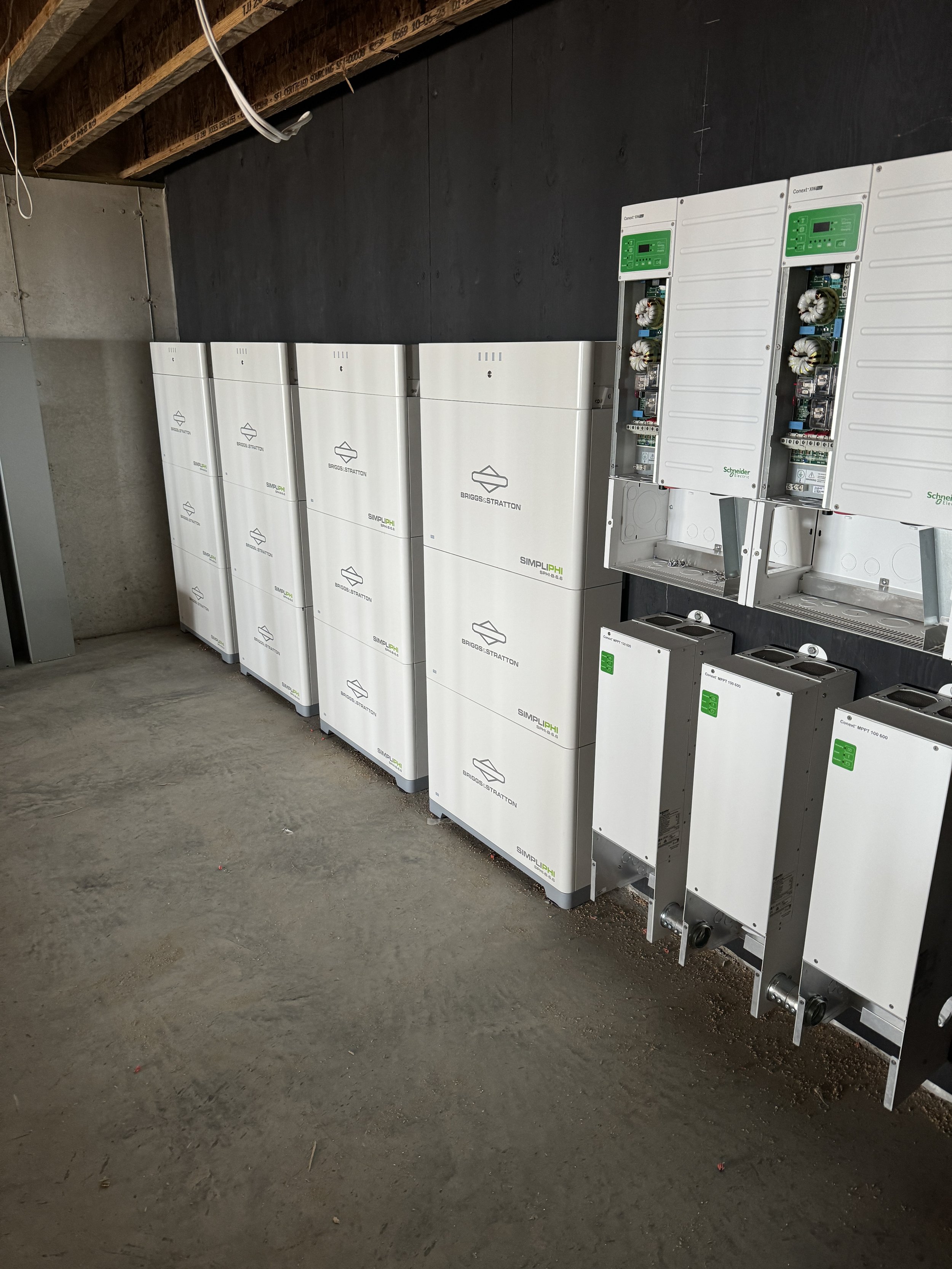 Arranged electrical units and control panels on a construction site with wooden beams and a concrete floor.