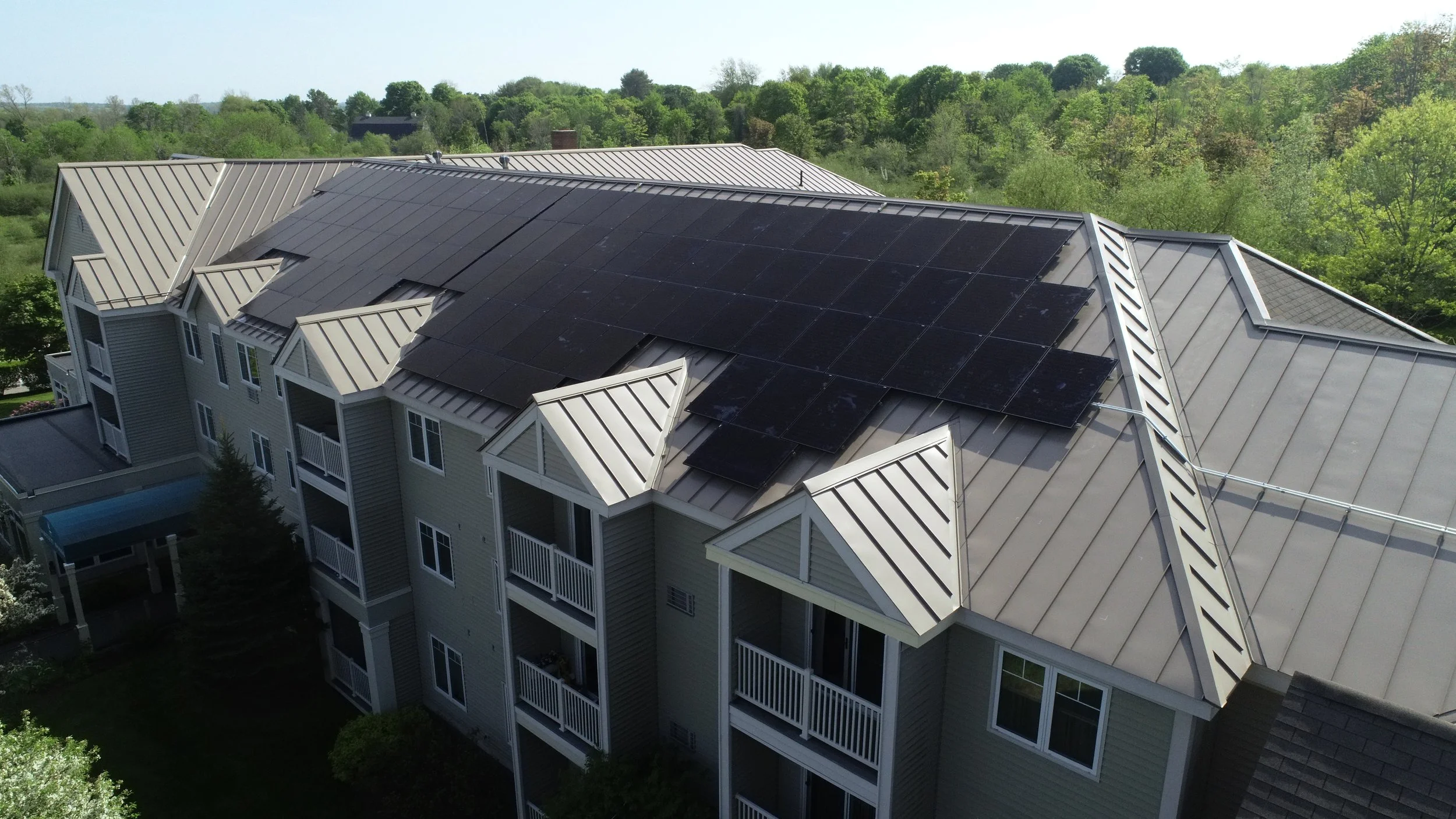 A residential building with beige siding and white balconies, featuring black solar panels installed on the roof.
