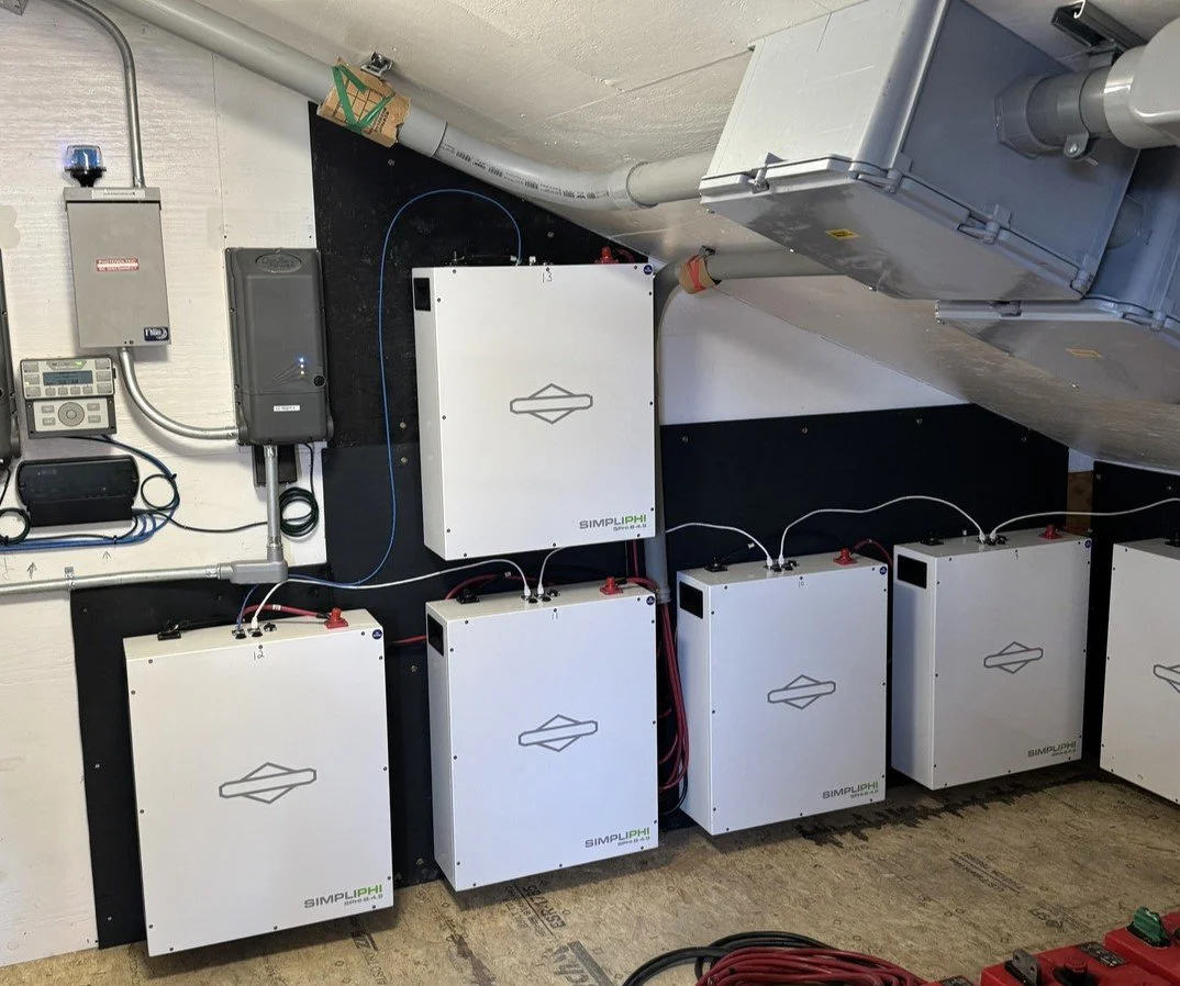 Multiple white electrical inverter boxes mounted on a black wall, connected by red and black wires, with various electrical components and conduit pipes above.