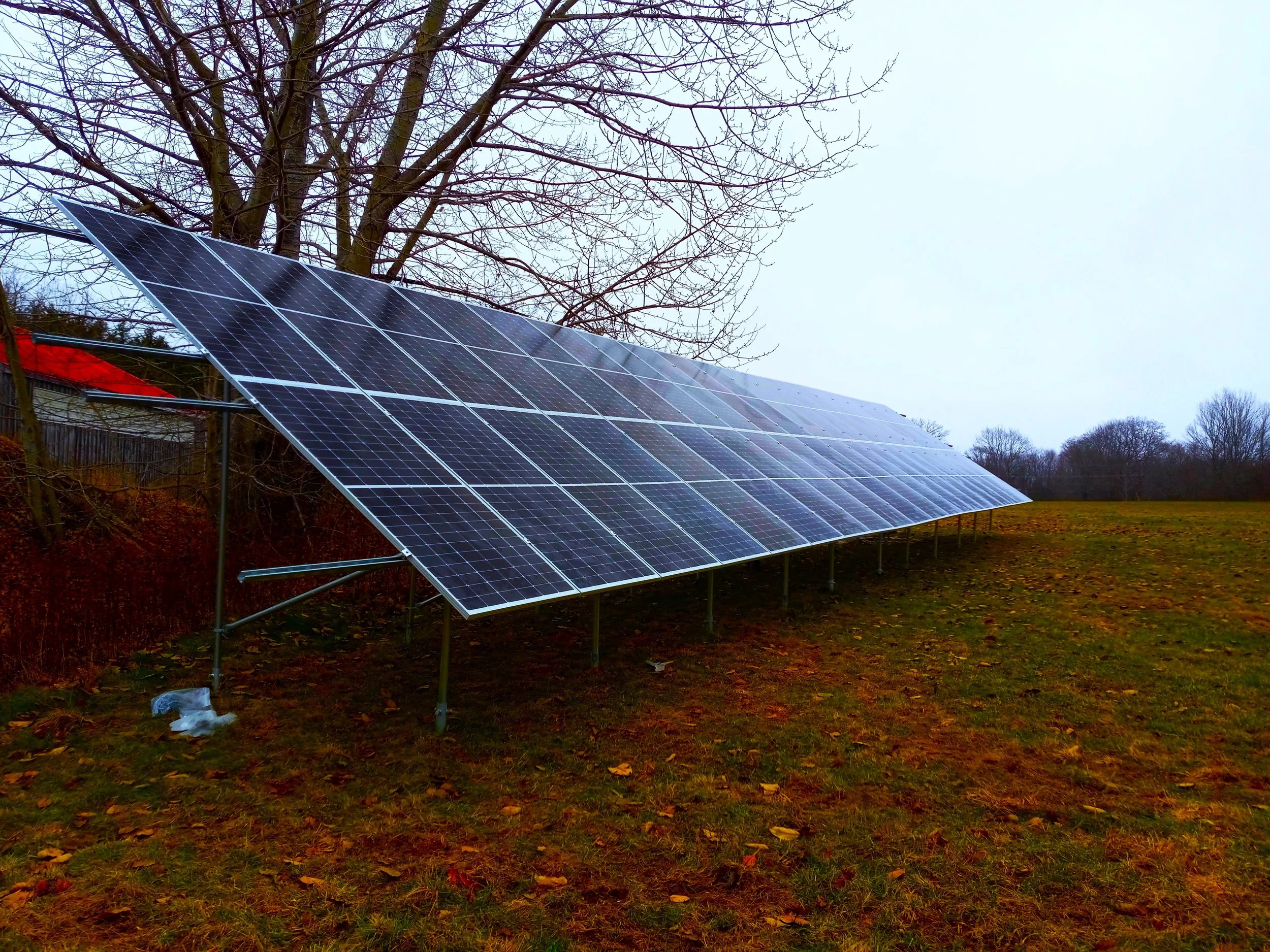 Solar panels installed on a stand in an outdoor area with trees and a cloudy sky in the background.