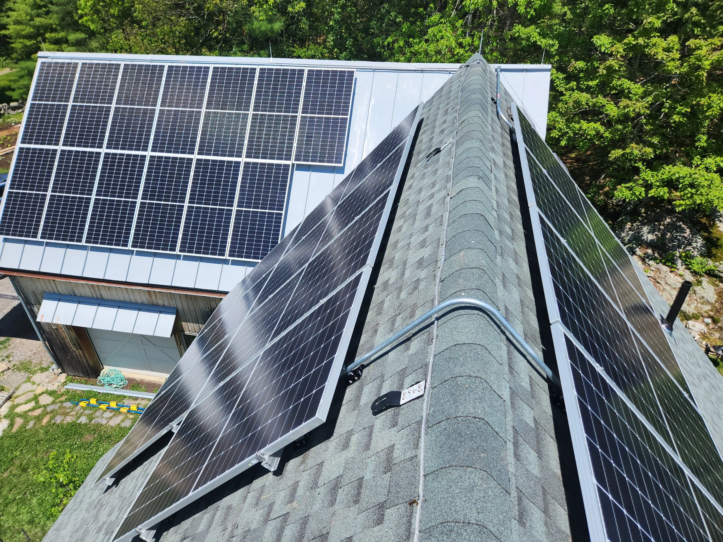 A house roof with multiple solar panels installed on it, surrounded by green trees.