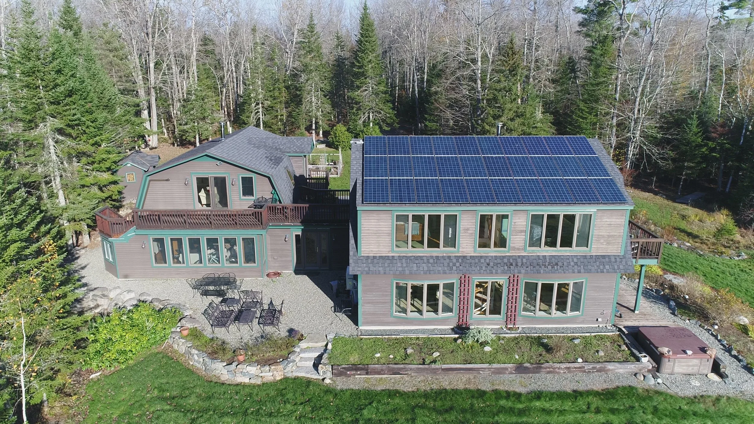 Aerial view of a house with solar panels on the roof, surrounded by trees and a backyard with outdoor furniture.