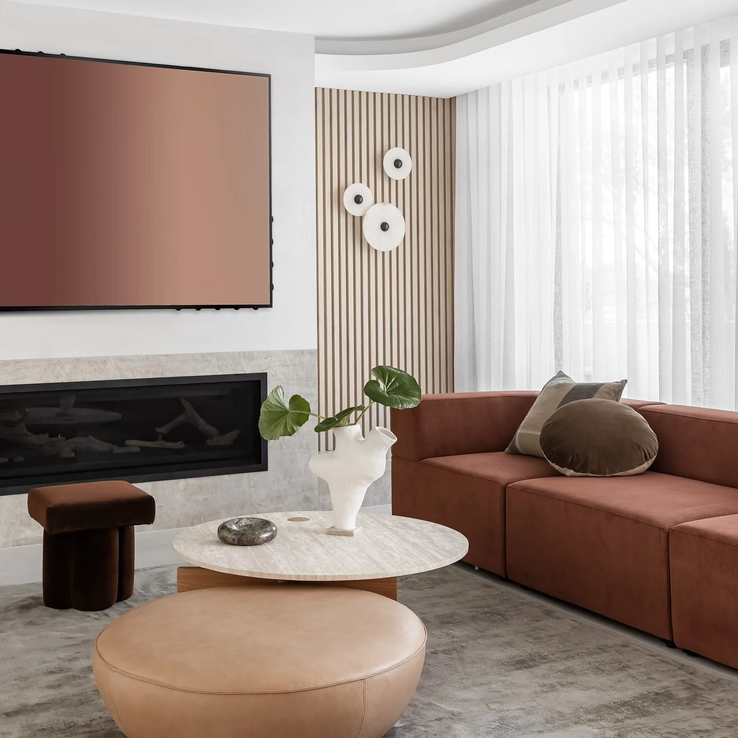 A calm, confident living space at Elevare Residence.
Custom vertical paneling brings quiet structure, with sculptural wall lights and a soft stone fireplace anchoring the room. Terracotta, rust, and caramel tones are layered over gentle neutrals, cre
