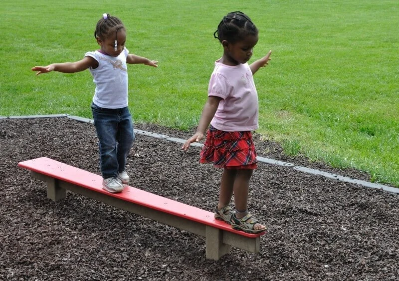 Two young girls pay on a balance beam, practicing their balance