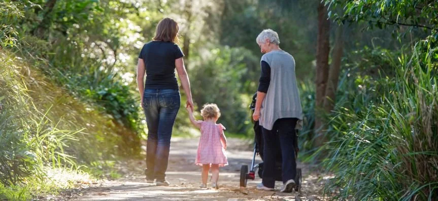 A senior woman walks with her daughter and grand daughter on a gravel path in the bush