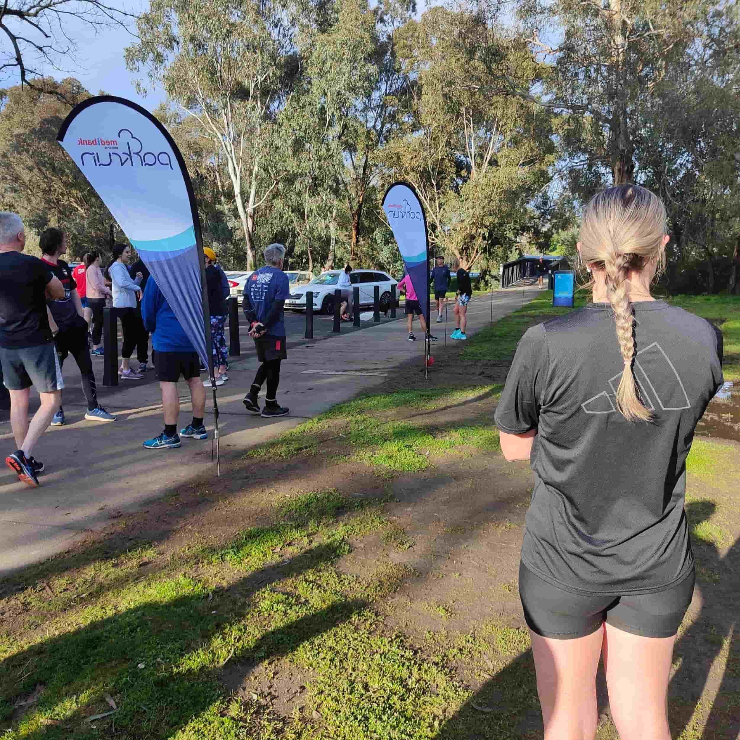 A woman stands confidently before a diverse group, embodying the spirit of community at Diamond Creek, Vic Parkrun event.