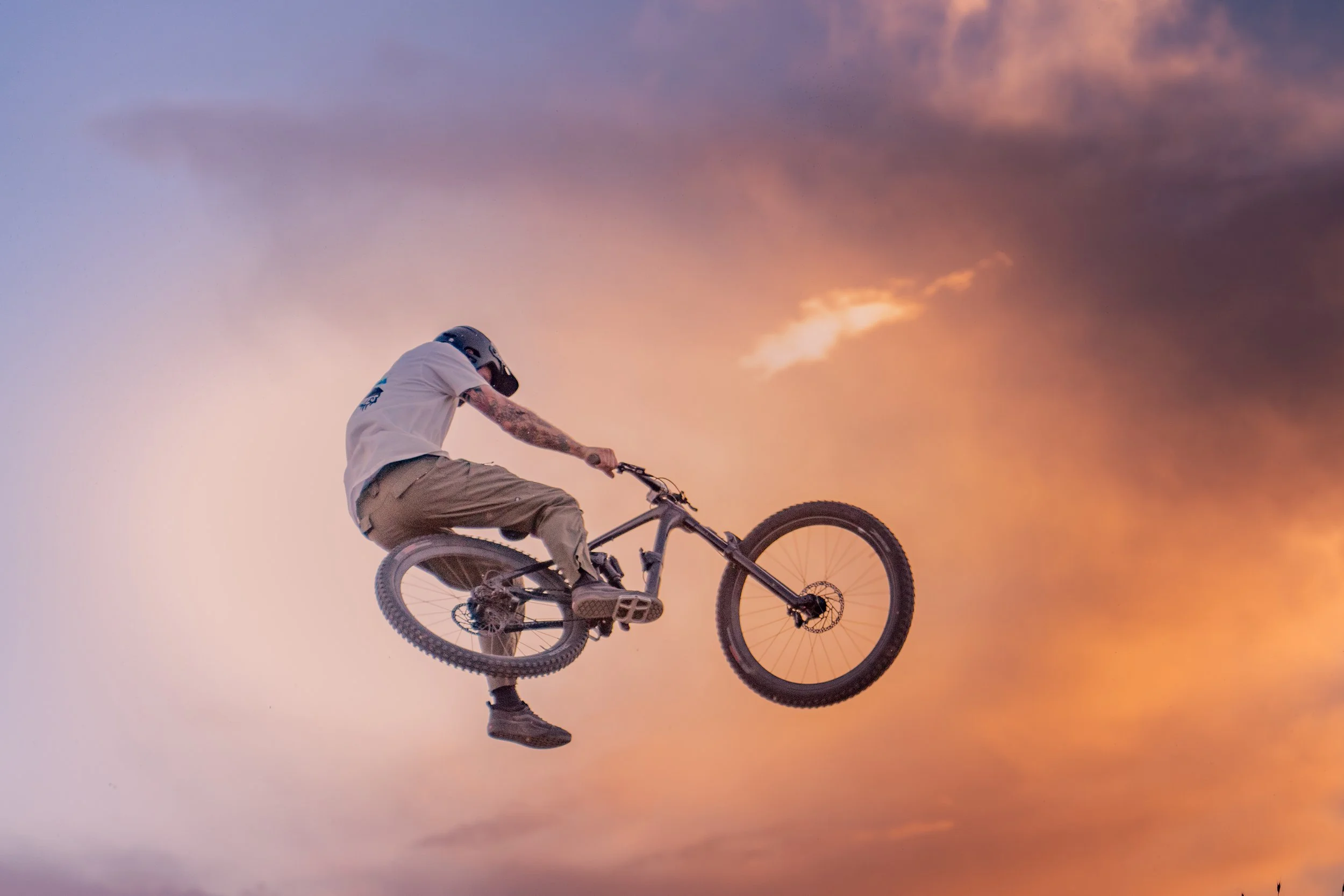 A biker performing a jump on a mountain bike against a sunset sky | Photography by Anders Henrikson Photo 