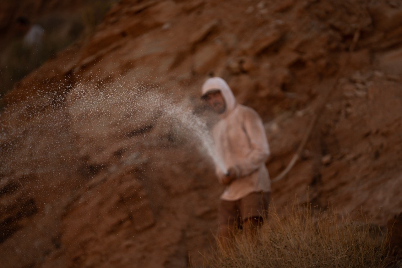 Person wearing a hoodie spraying white powder against a rocky background.