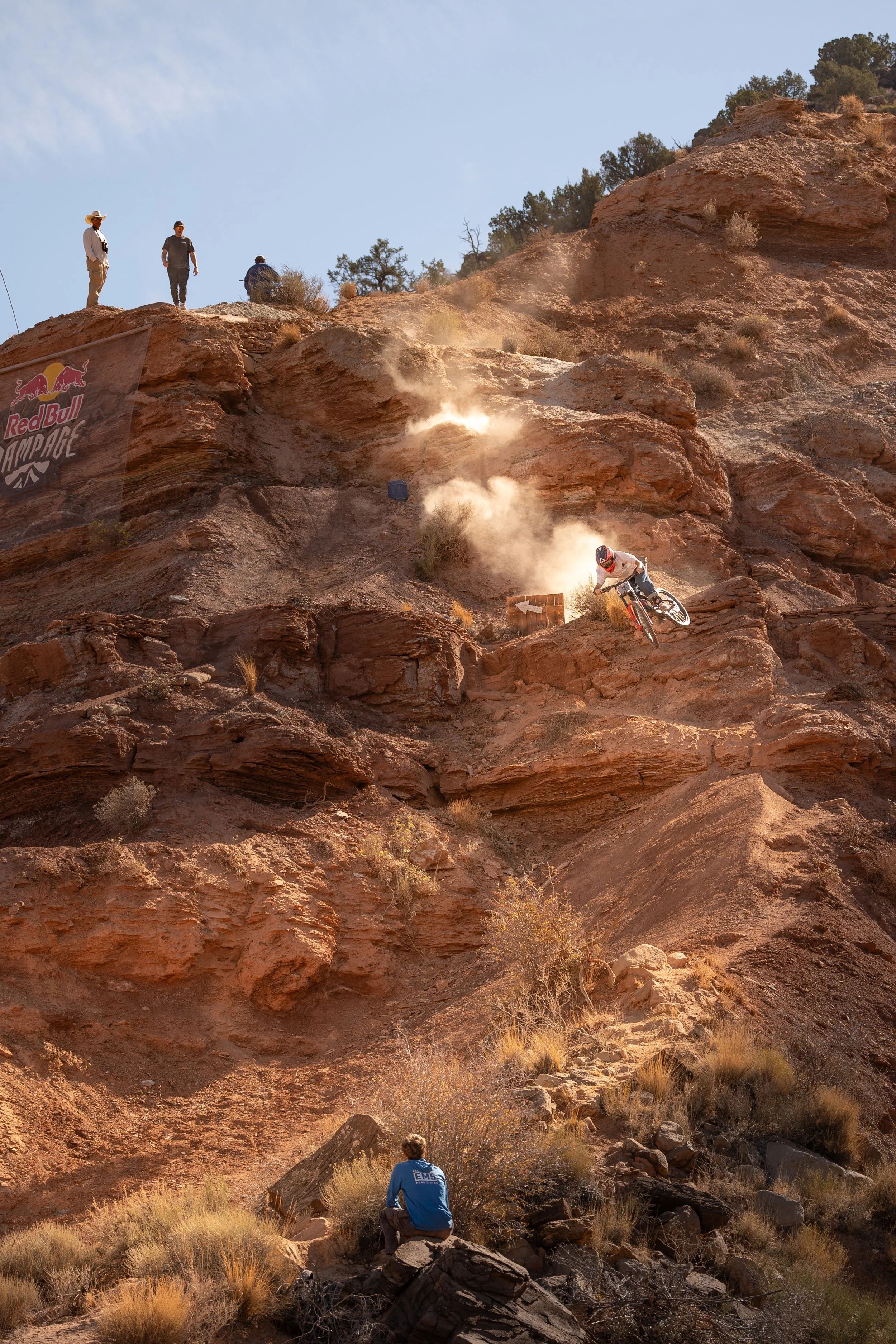 Mountain biker descending a rocky slope at Red Bull Rampage event, with spectators watching from above.