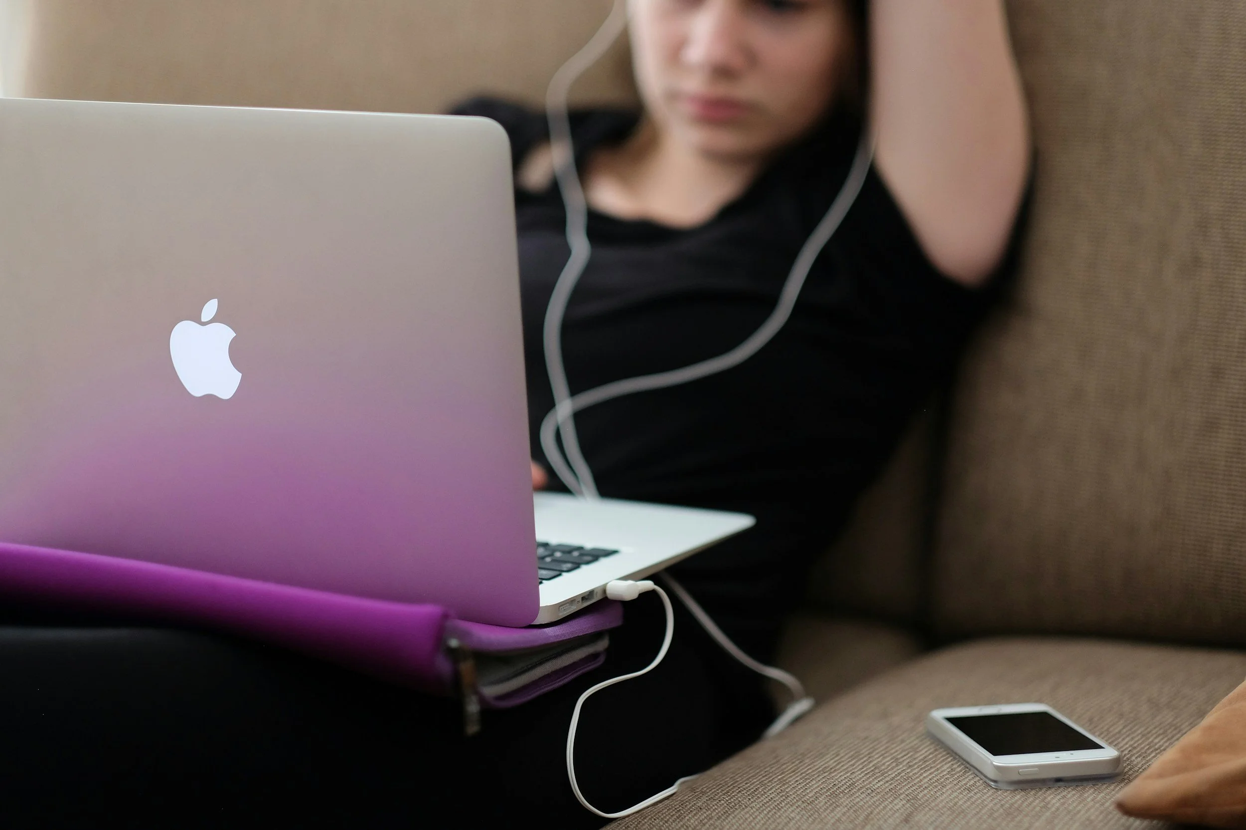 Girl sitting on couch wearing headphones and using a laptop