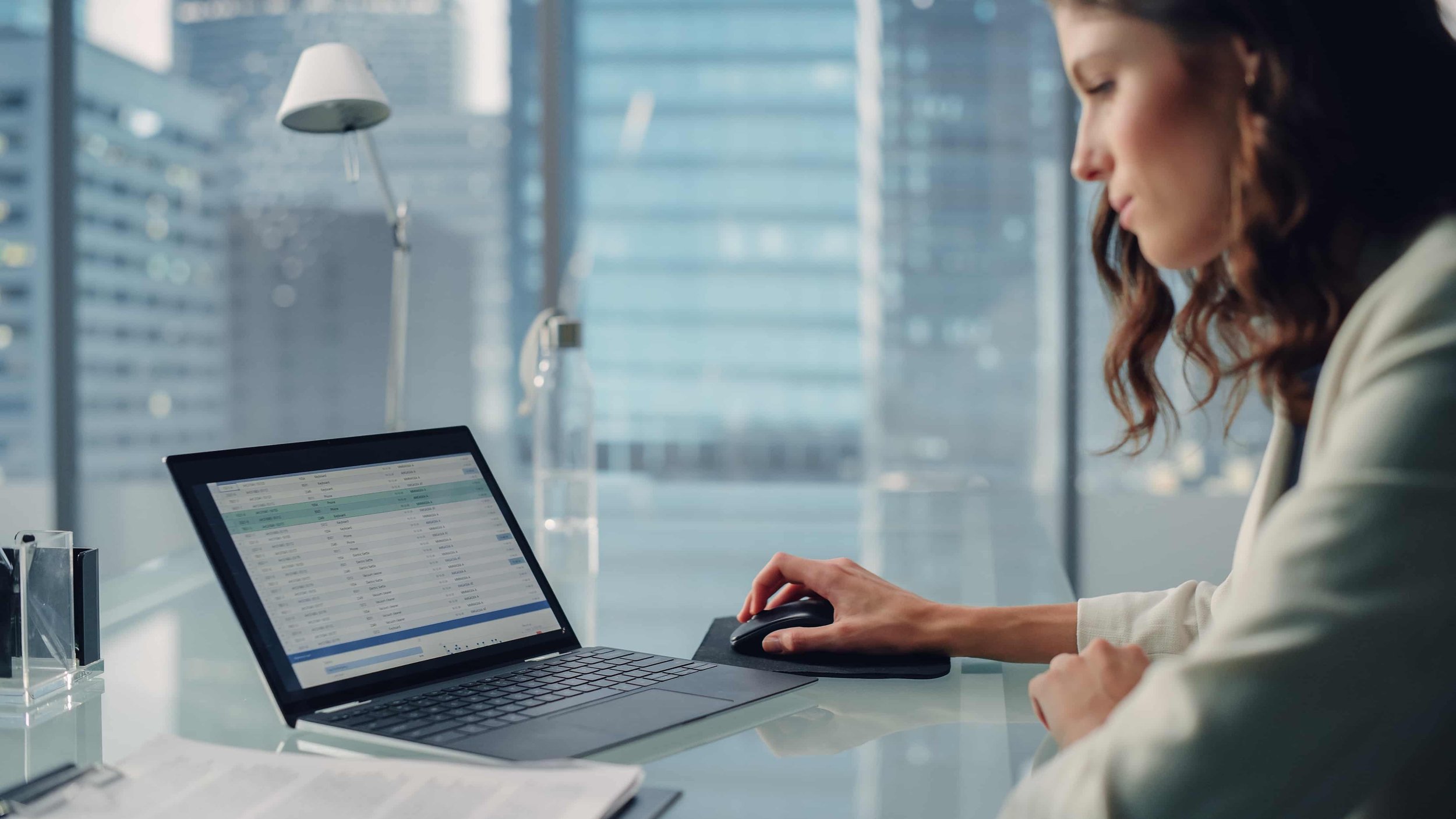 A sales professional entering data into a CRM system on her laptop, while sitting in an office