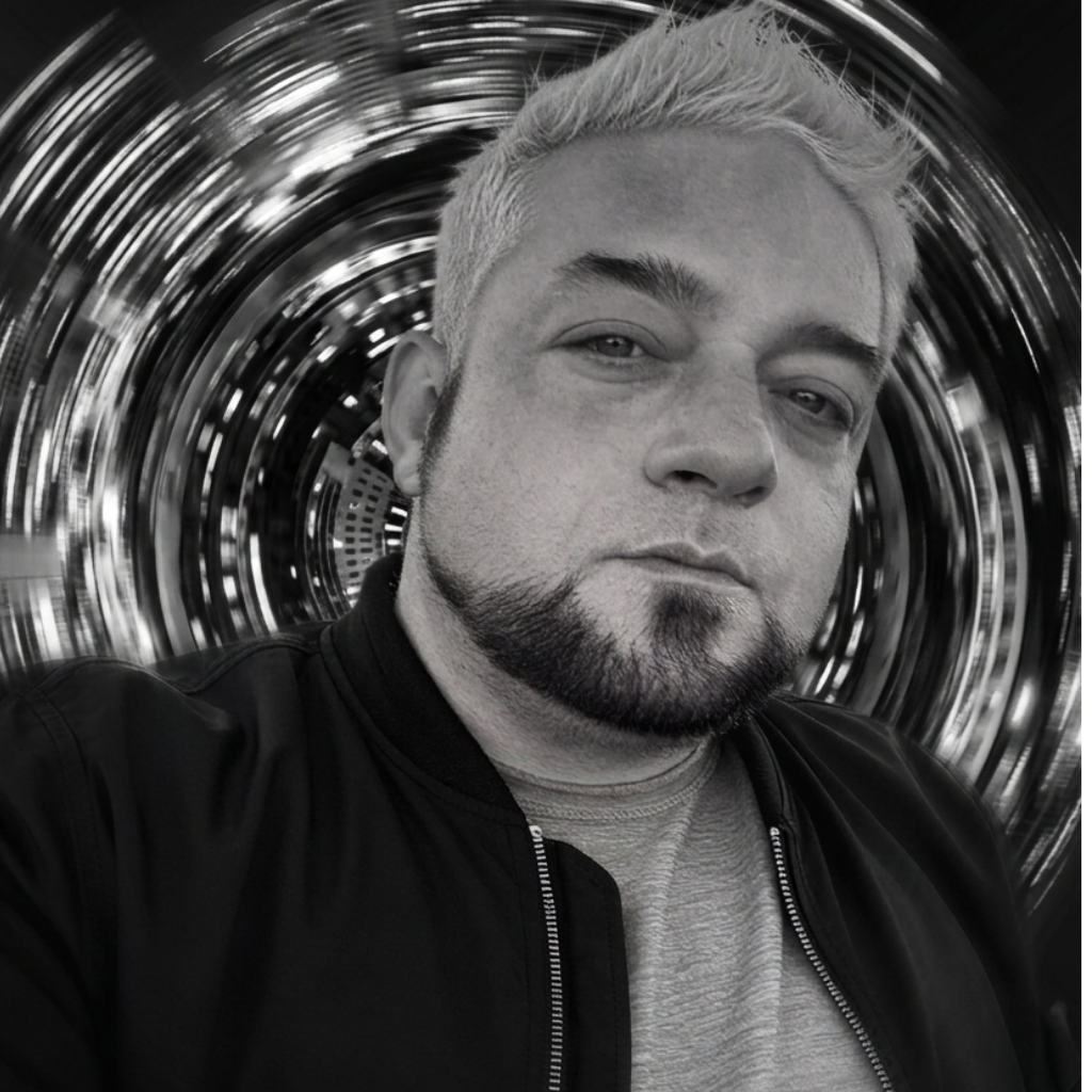 Black and white selfie of international superstar DJ Trey Triplicate with dyed light hair, a goatee, and a serious expression, standing in front of a spiral motion-blurred background. He looks very handsome, and demure.