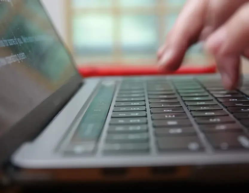 Close-up of a person's fingers typing on a laptop keyboard with a blurred background.