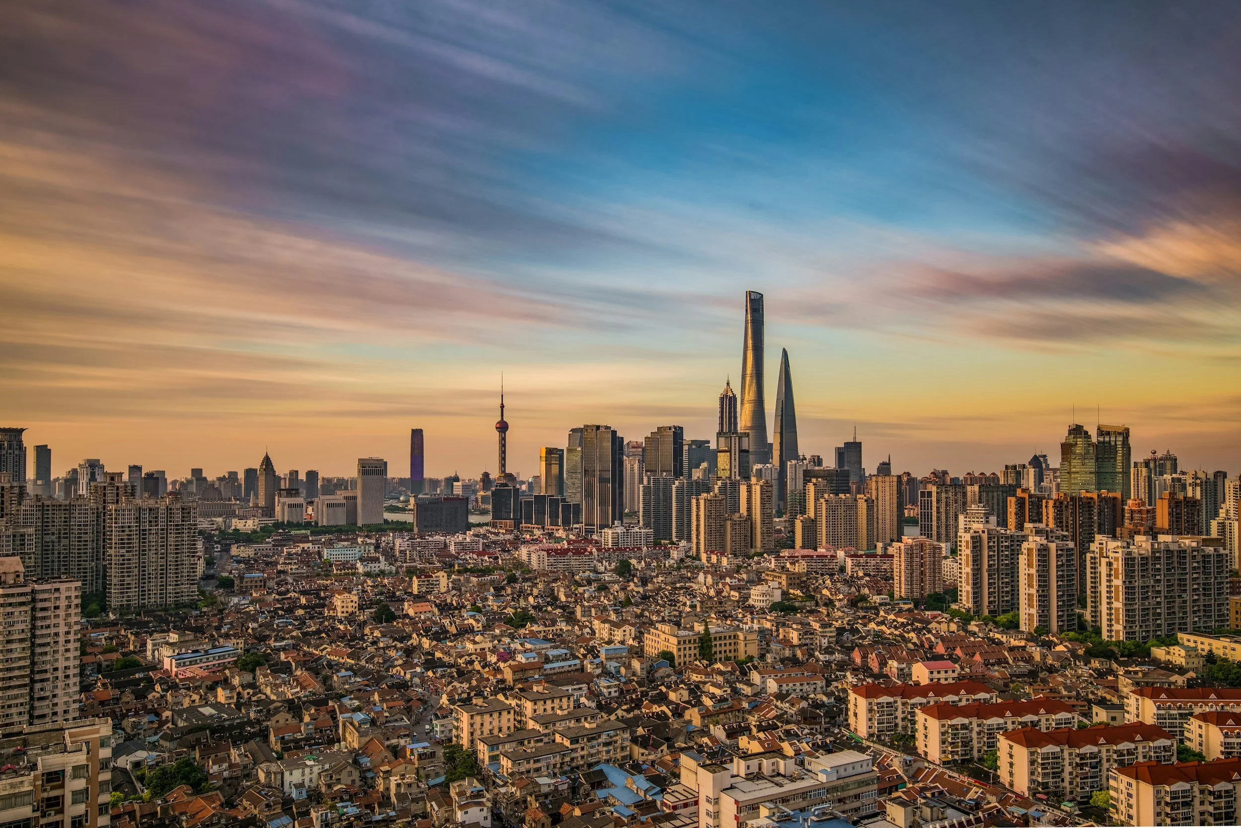 A city skyline at sunset with tall skyscrapers, including the Shanghai Tower, Jin Mao Tower, and Shanghai World Financial Center, in Shanghai, China.