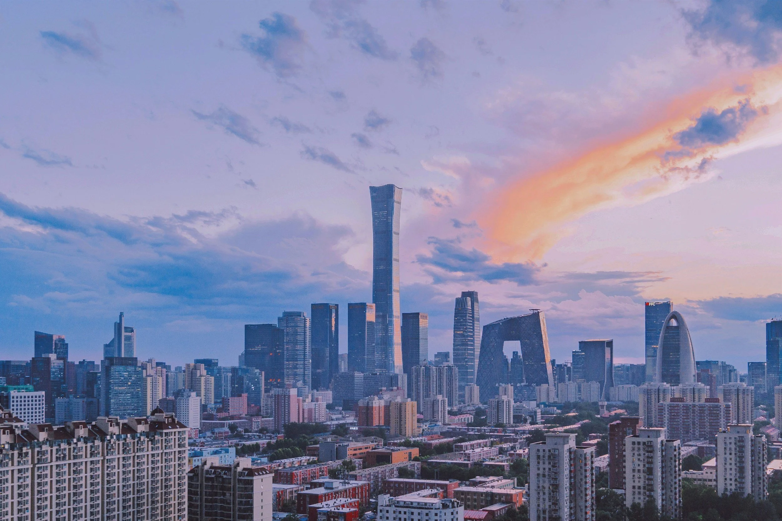 Skyline einer Stadt mit hohen Wolkenkratzern bei Sonnenuntergang oder Sonnenaufgang, mit bunten Wolken am Himmel.