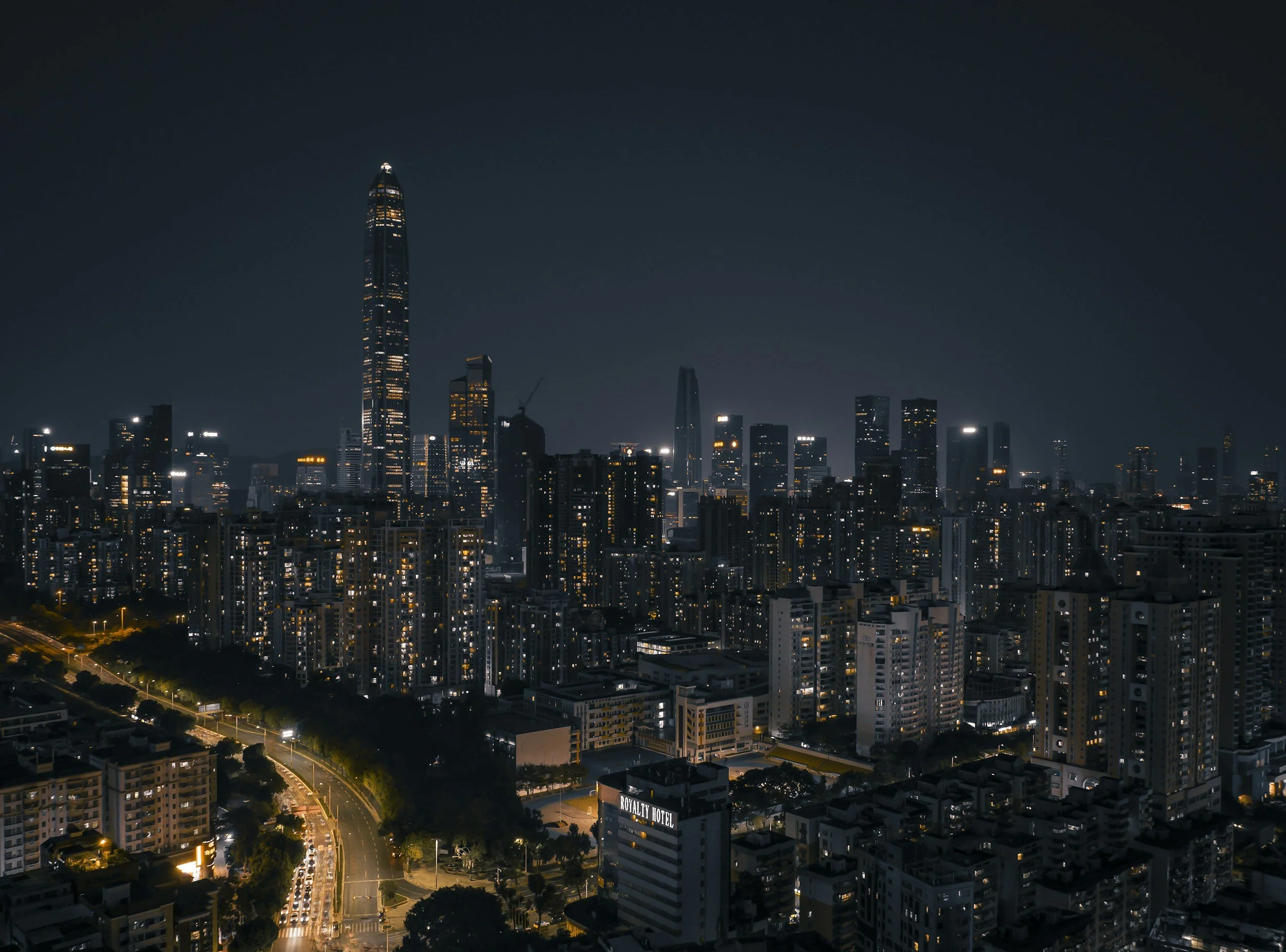 Nighttime cityscape of a densely populated urban area with illuminated skyscrapers and mid-rise buildings, featuring the tall, narrow skyline of the city.