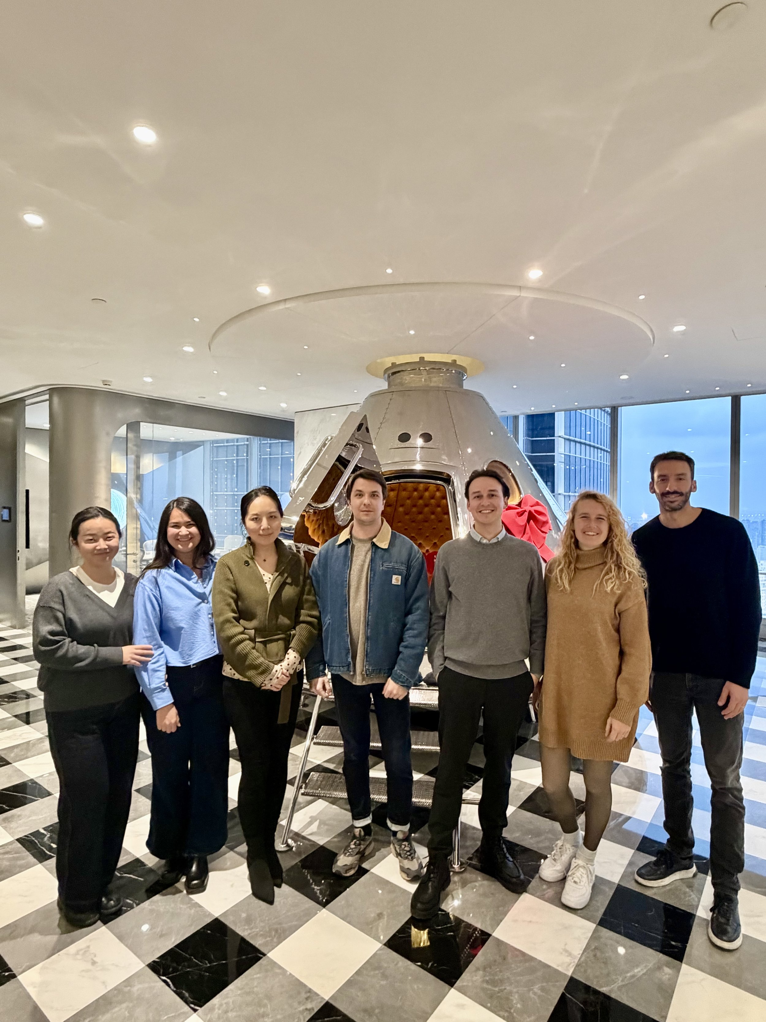 Group of seven people standing inside a building near a lunar module replica.