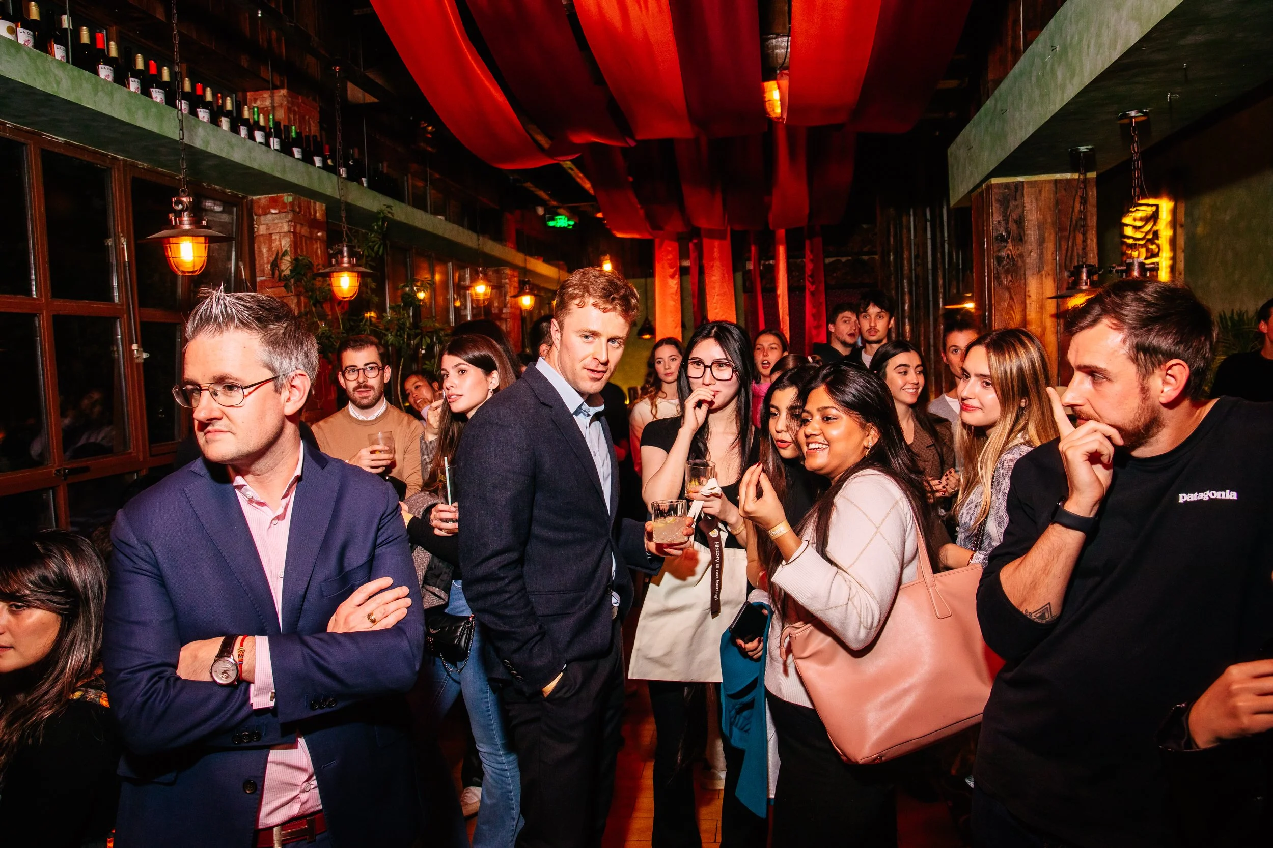 Group of people socializing at a party or social gathering in a warmly lit bar or restaurant.