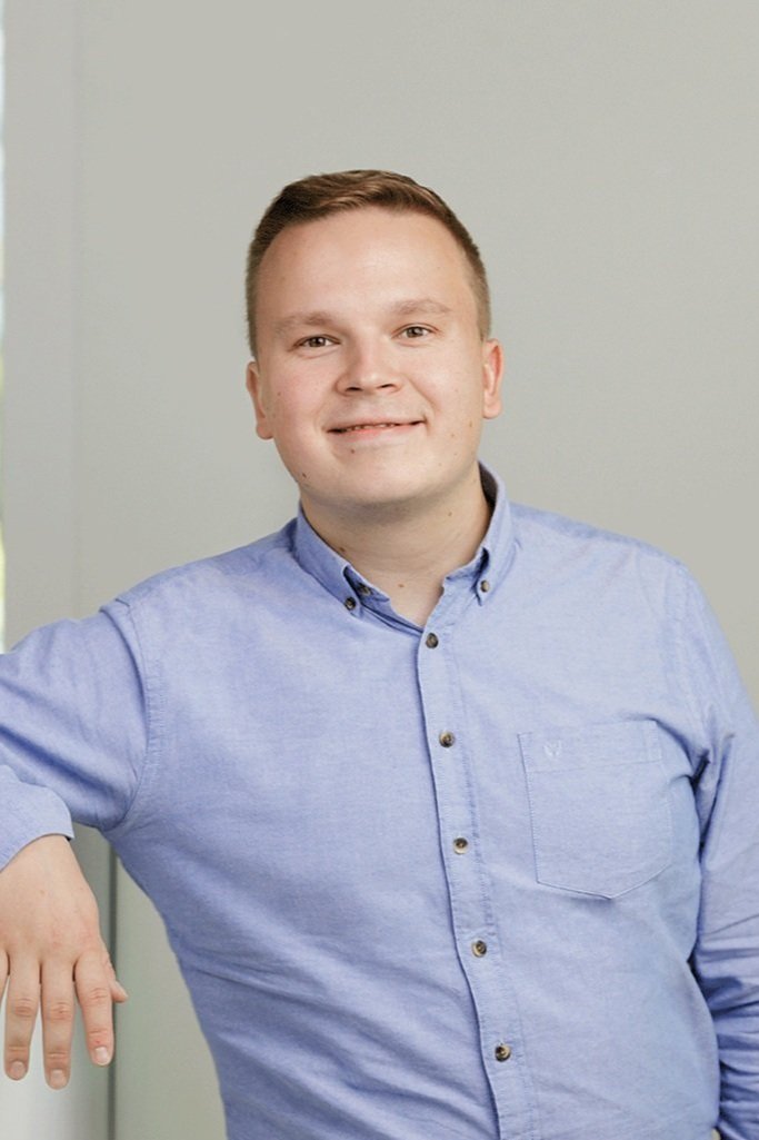 Nuori mies sinisessä puserossa hymyilee kameralle.