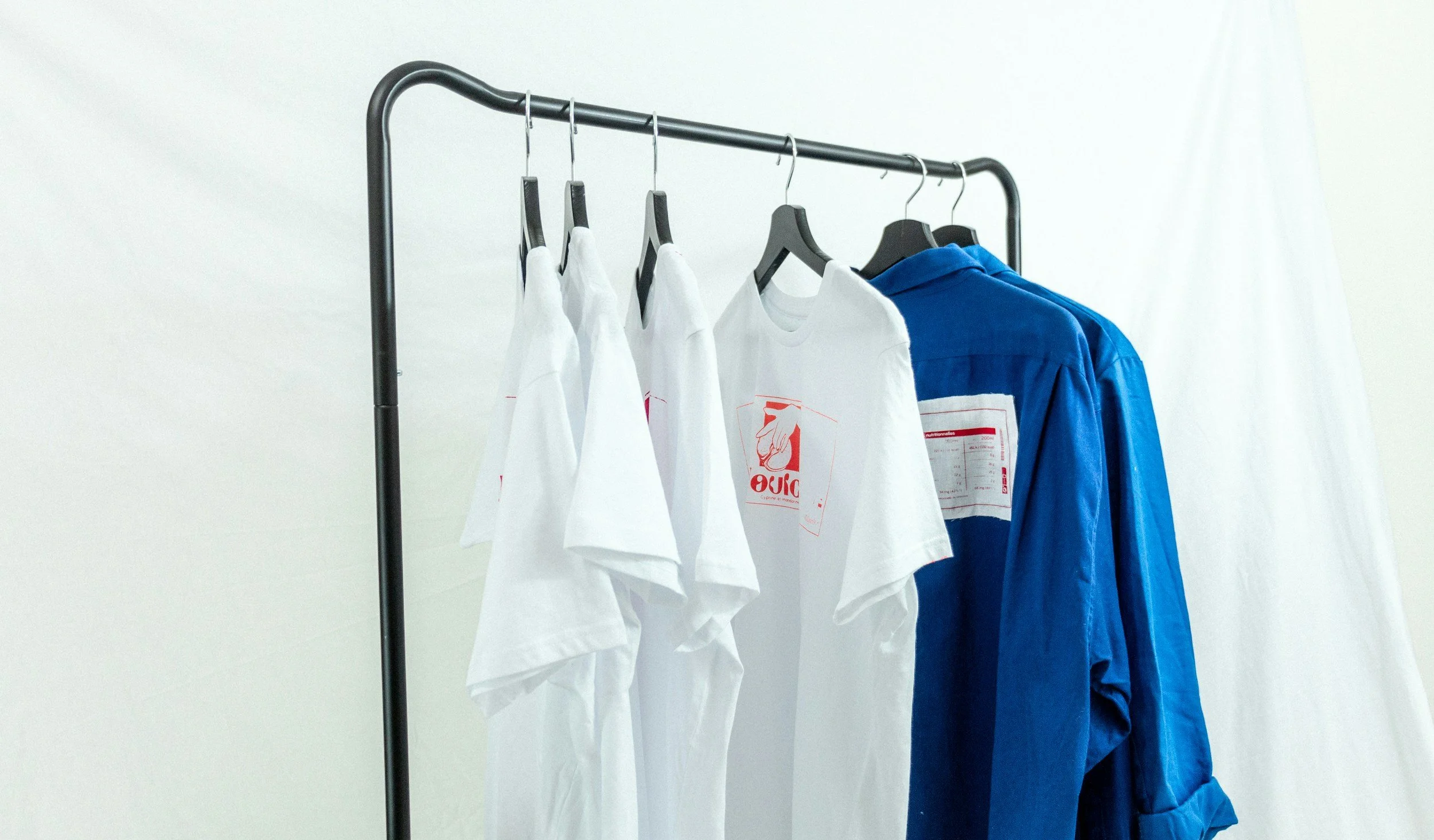 Clothing rack holding white T-shirts and blue long-sleeve shirts against a plain background.