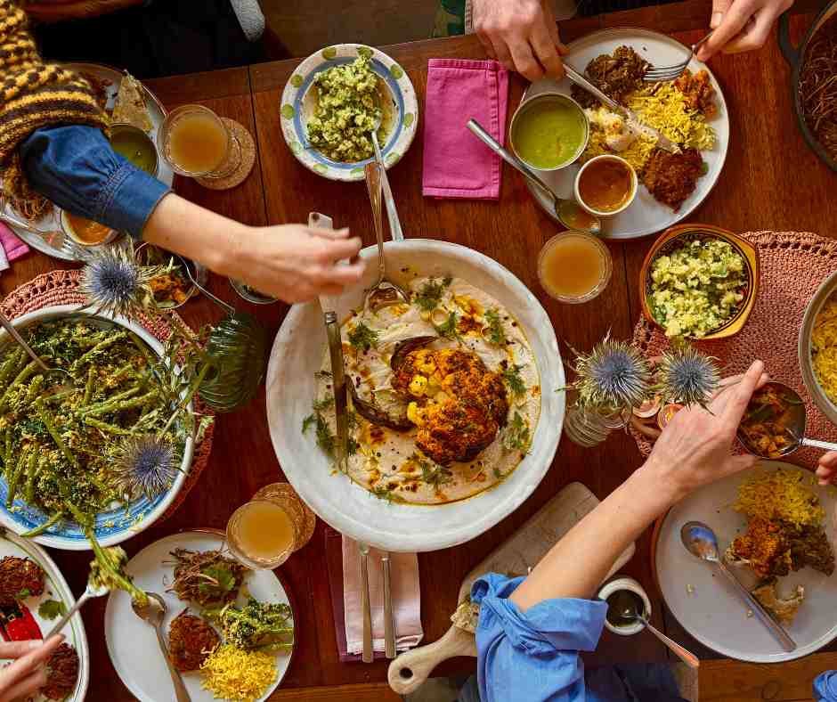 feast of vegan dishes on a table with people's hands reaching
