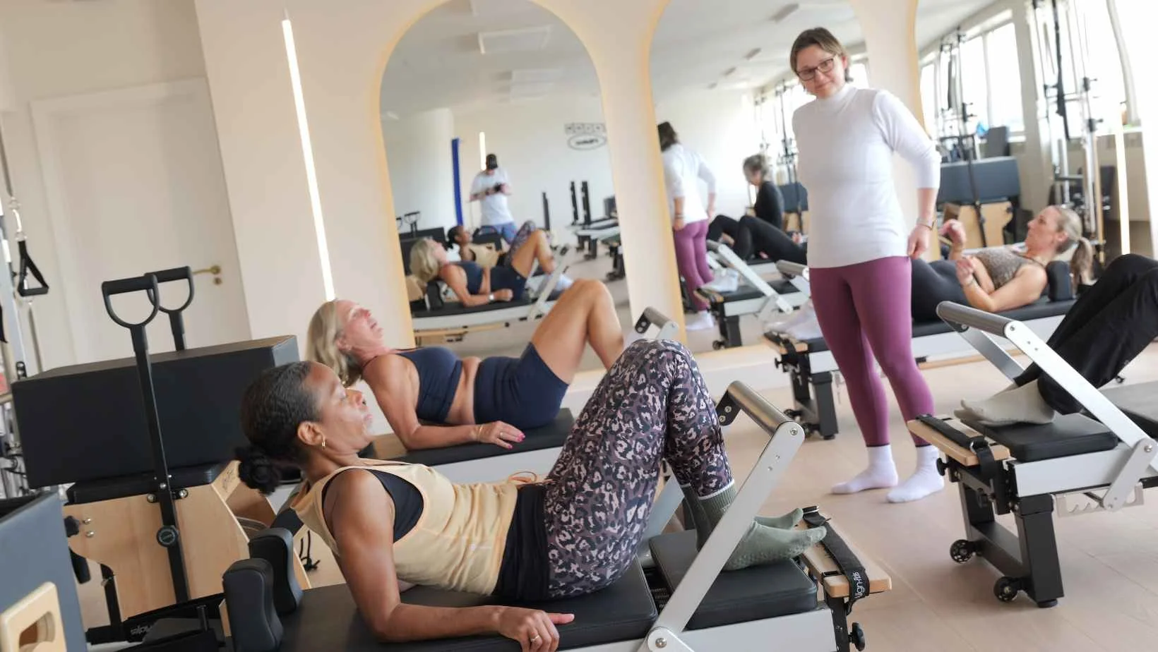 women on reformer pilates machines in a light studio