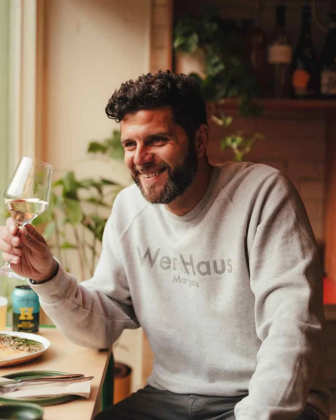 man with beard sits in the window drinking wine