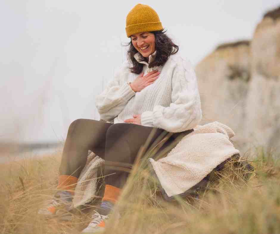 woman in outdoor wear sitting on a beach in a yellow hat