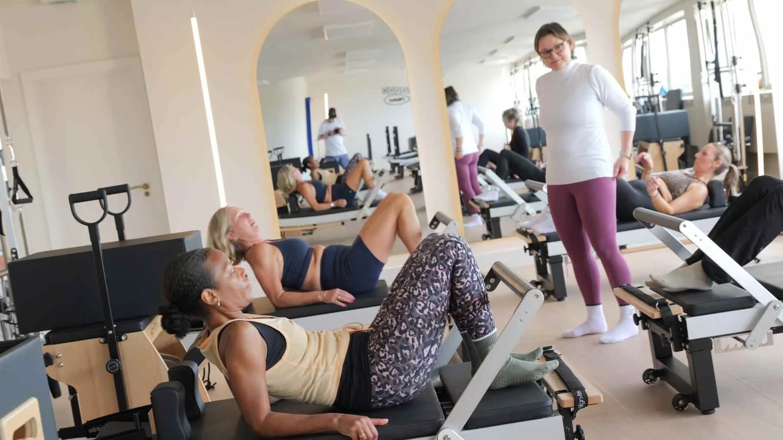 women on reformer machines in a light studio